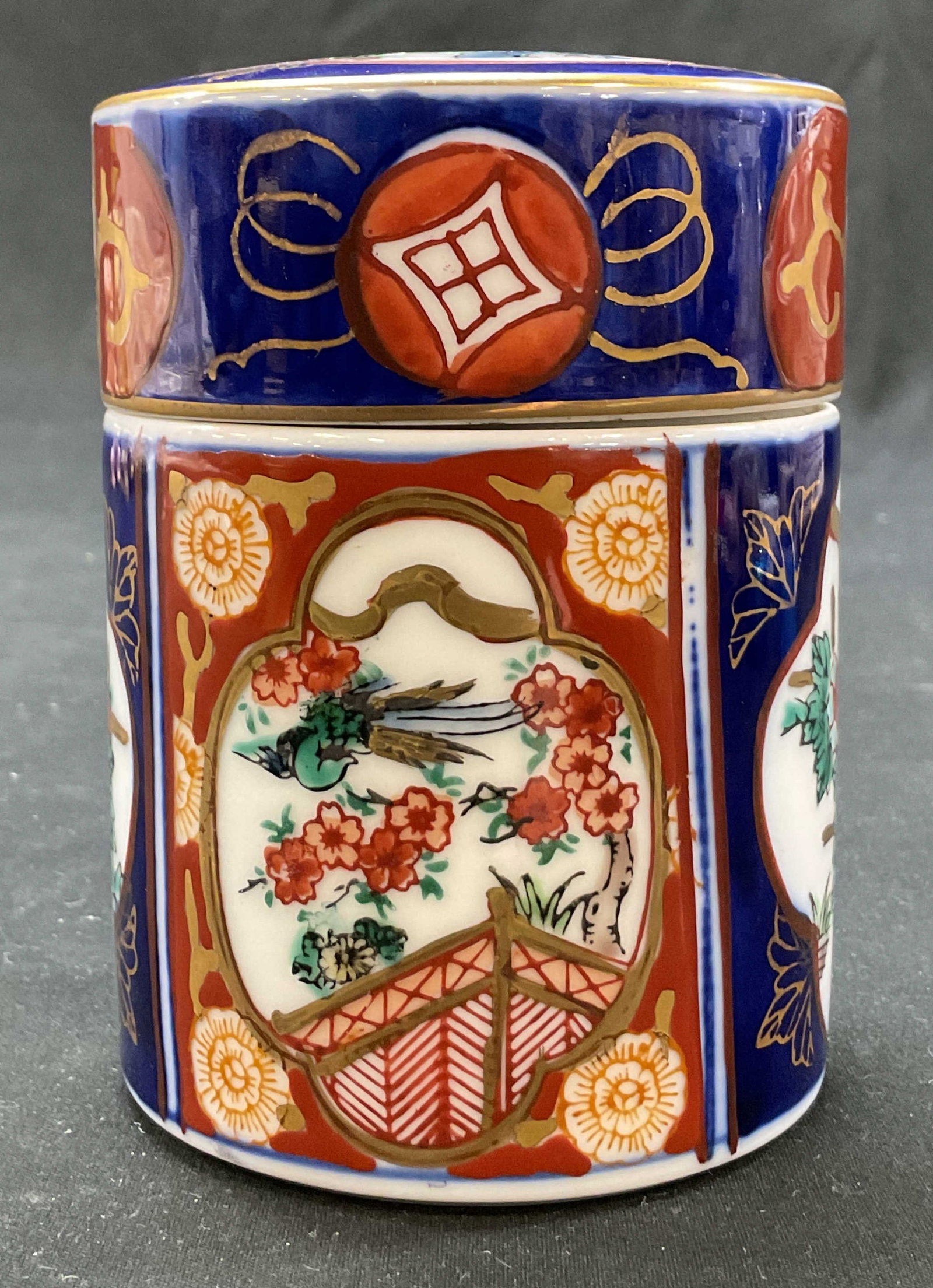 Gold Imari Porcelain Ginger Jar Japan: Gold Imari porcelain ginger jar. Marked on underside, reads Gold Imari Hand Painted Japan. Cylindrical shape with lid. Imari pattern, floral architecture and bird motifs in varying colors. Gilt accent