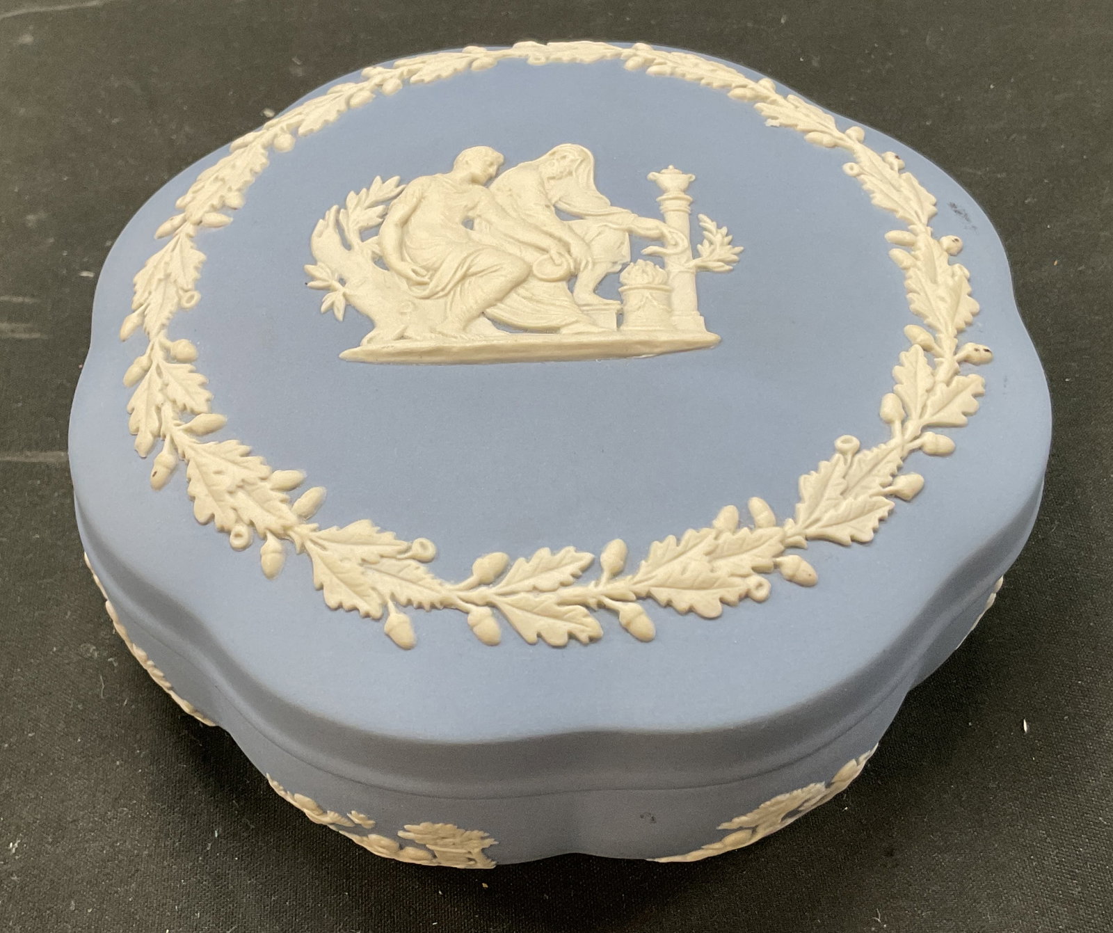 Wedgwood Blue Jasperware Trinket Box England: Wedgwood blue Jasperware lidded trinket box. Marked on underside, faintly reads Wedgwood England. Scalloped edge. Matte finish. Pale blue color. Embossed figural and leaf motifs. Neoclassical decorati