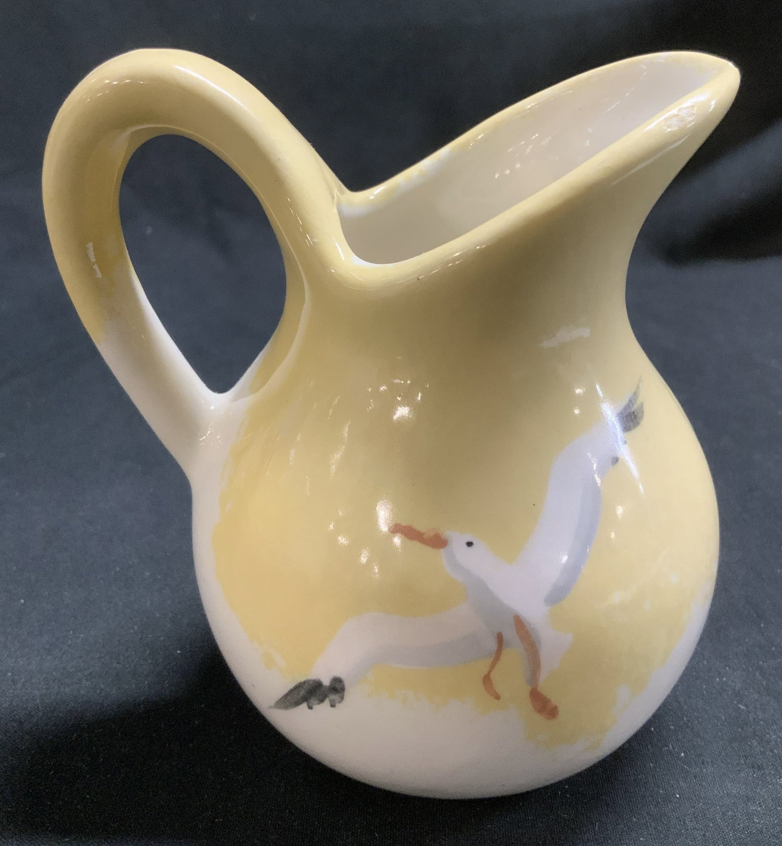 Sgnd Hand Painted Seagull Creamer: Creamer features a hand painted seagull motif. Yellow, white, black & orange toned. Signed & marked on underside. Reads, Jobi. Surface wear consistent to age, use & exposure. Measurements: length 2.7i