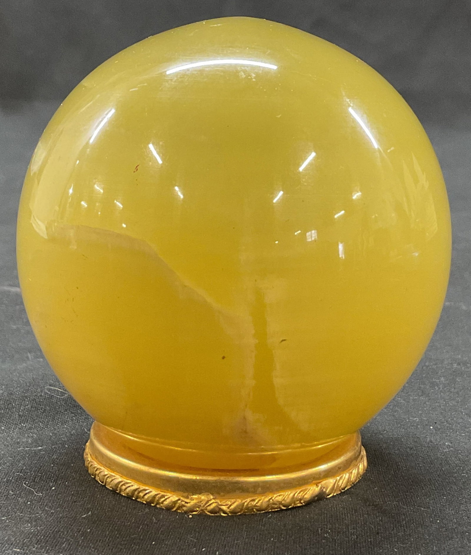 Polished Stone Sphere On Brass Toned Stand Italy: Polished stone sphere on brass toned stand. Marked made in Italy. Solid stone. Bright yellow color. Circular base stand with embossed ornate scroll motifs. Measures ht approx 3 inches base diam approx