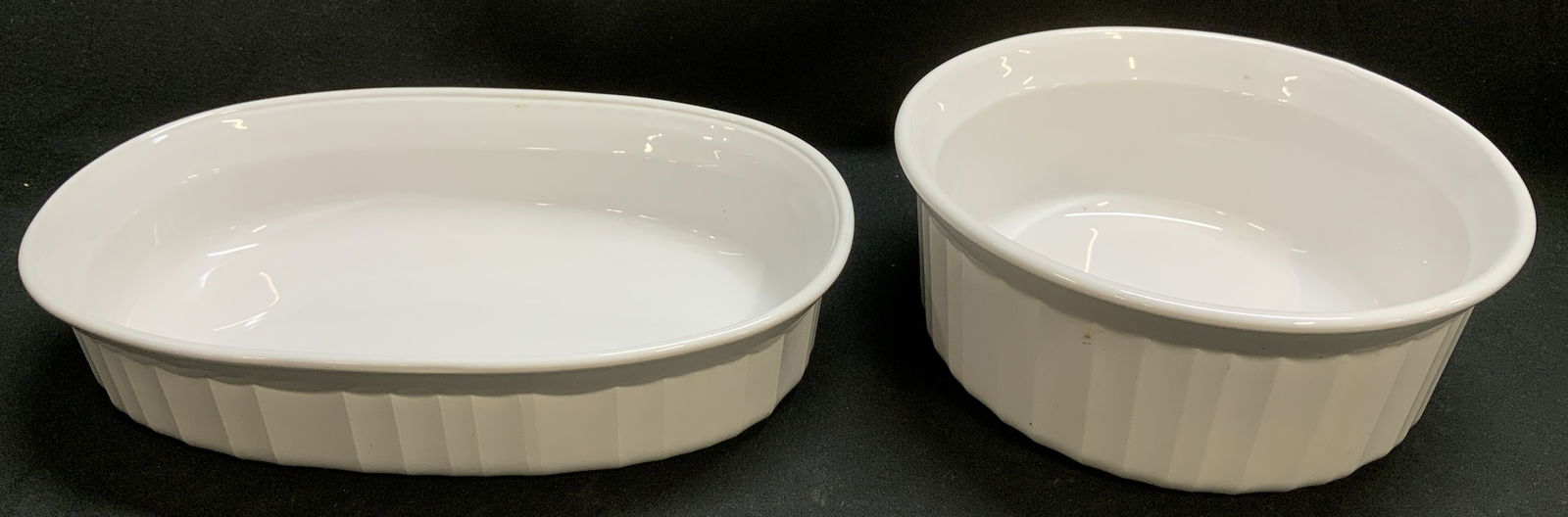 Lot 2 Corning Ware Ceramic Casserole Dishes: Lot includes, 2 Corning Ware ceramic casserole dish featuring an oval & round shape. White toned. Signed & marked on underside. Reads, CORNING WARE. Surface wear consistent to age, use & exposure. Mea