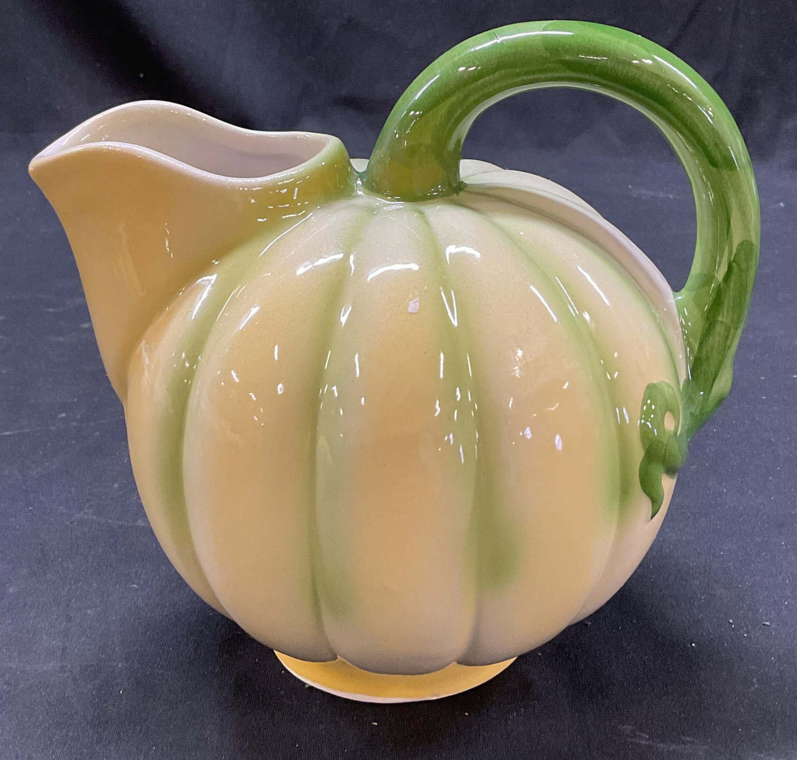 Vintage Ceramic Majolica Pumpkin Pitcher: Vintage ceramic majolica pumpkin pitcher. Bulbous and ribbed body. Yellow body and green accented handle. Swirled design. Hand painted. Glossy finish. Measures approx 6 x 8 x 5 inches. Some scratching