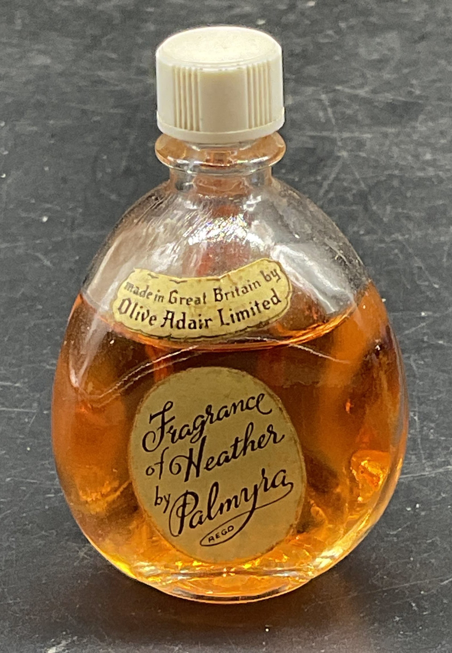 1950s Olive Adair Palmyra Heathers Perfume Britain: Vintage circa 1950s Olive Adair Fragrance of Heathers by Palmyra perfume in glass bottle. Made in Britain. Measures approx. 1 3/8 x 2 3/8 inches. As Is. Contents not examined. Some scratching. Olive A