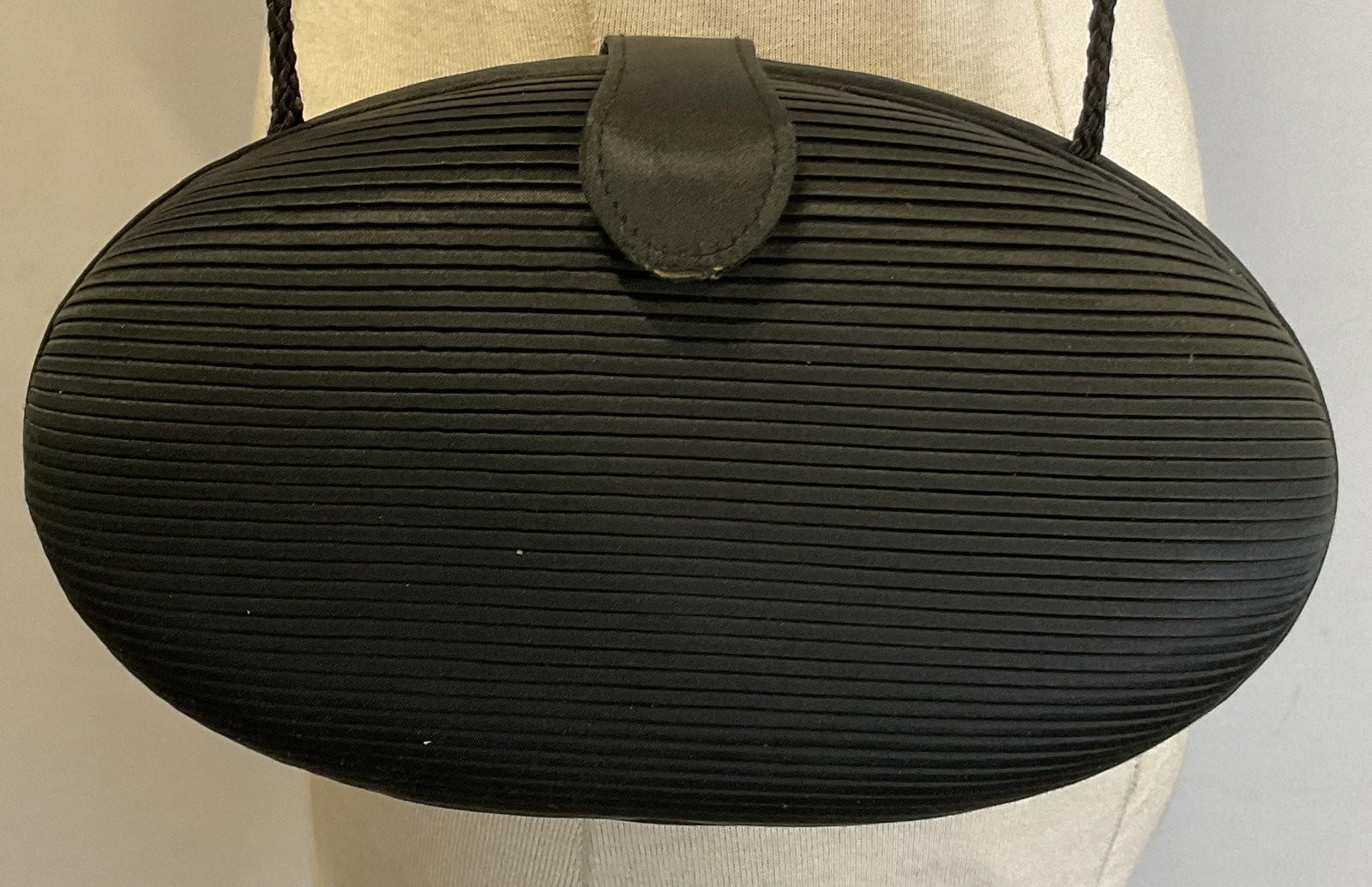 Vintage Black Oval Shaped Clutch Purse: Vintage black oval shaped clutch purse. Oval shape. Ribbed pleated surface. Brass toned button closure. Attached strap. Opens to interior compartments. Measures approx 6.5 x 9.5 inches. Purse, clutch