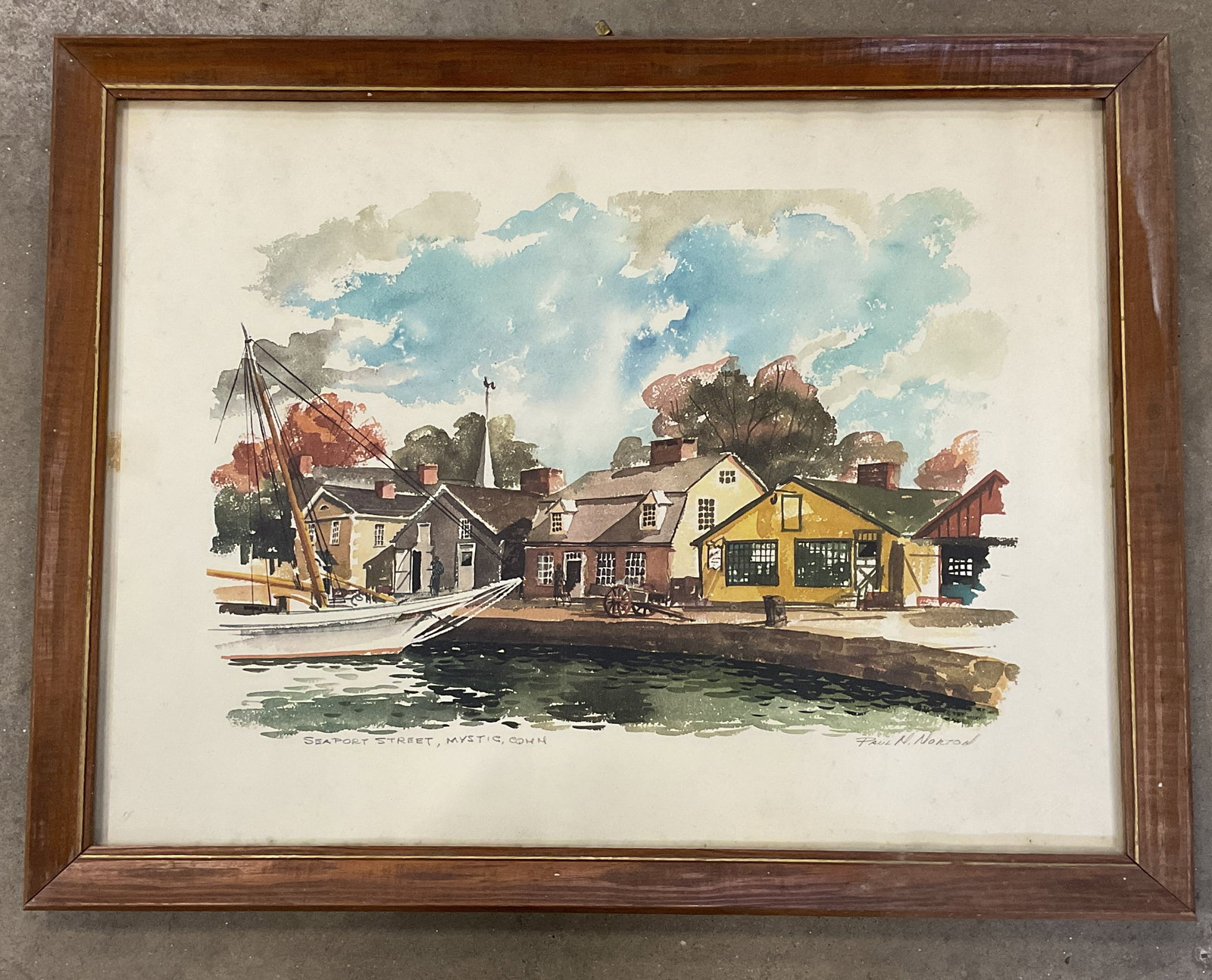 Framed Norton Mystic Seaport Lithograph 26in: Framed lithograph on paper. After Paul N Norton, Seaport Street, Mystic, Connecticut. Boat and buildings. Woof frame. Not examined out of frame. Frame measures approx. 20.5 x 26.5 inches. Wear includi