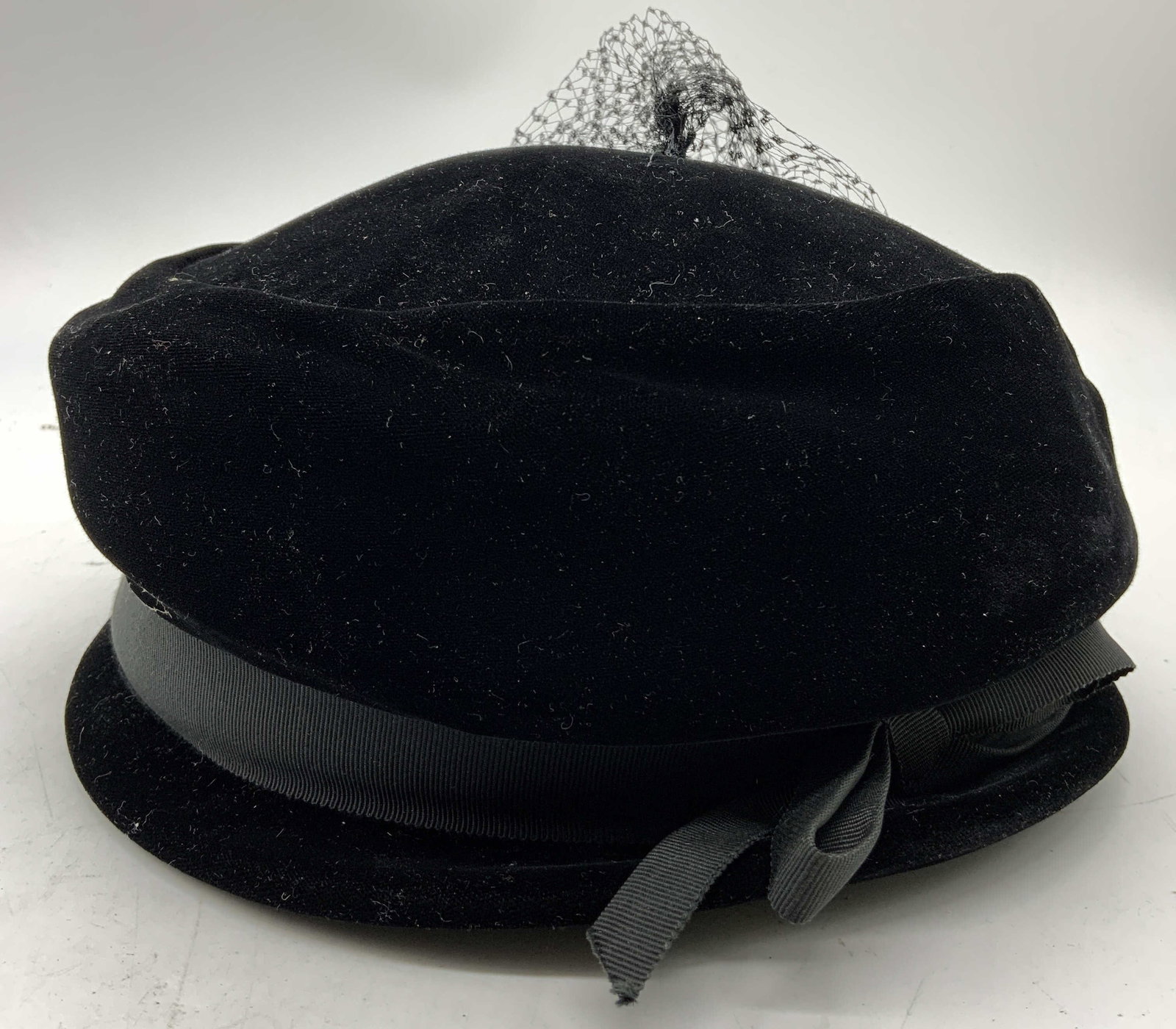 Vtg Black Velvet Womens Pillbox Hat Medium: Pillbox hat is black toned and velvet piece has black toned band around crown tied into a bow. Backside of hat has netting. Interior is green toned. Tag reads MEDIUM. Hat measures approximately 7 inch