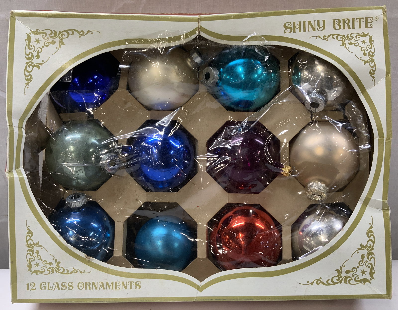 Set 12 Shiny Brite Glass Ornaments W Org Box: Lot includes, 12 glass ornaments featuring a round shape. Purple, blue, grey, red. American Made. Comes with original box. Surface wear consistent to age, use & exposure. Signed & marked. Reads, Shiny