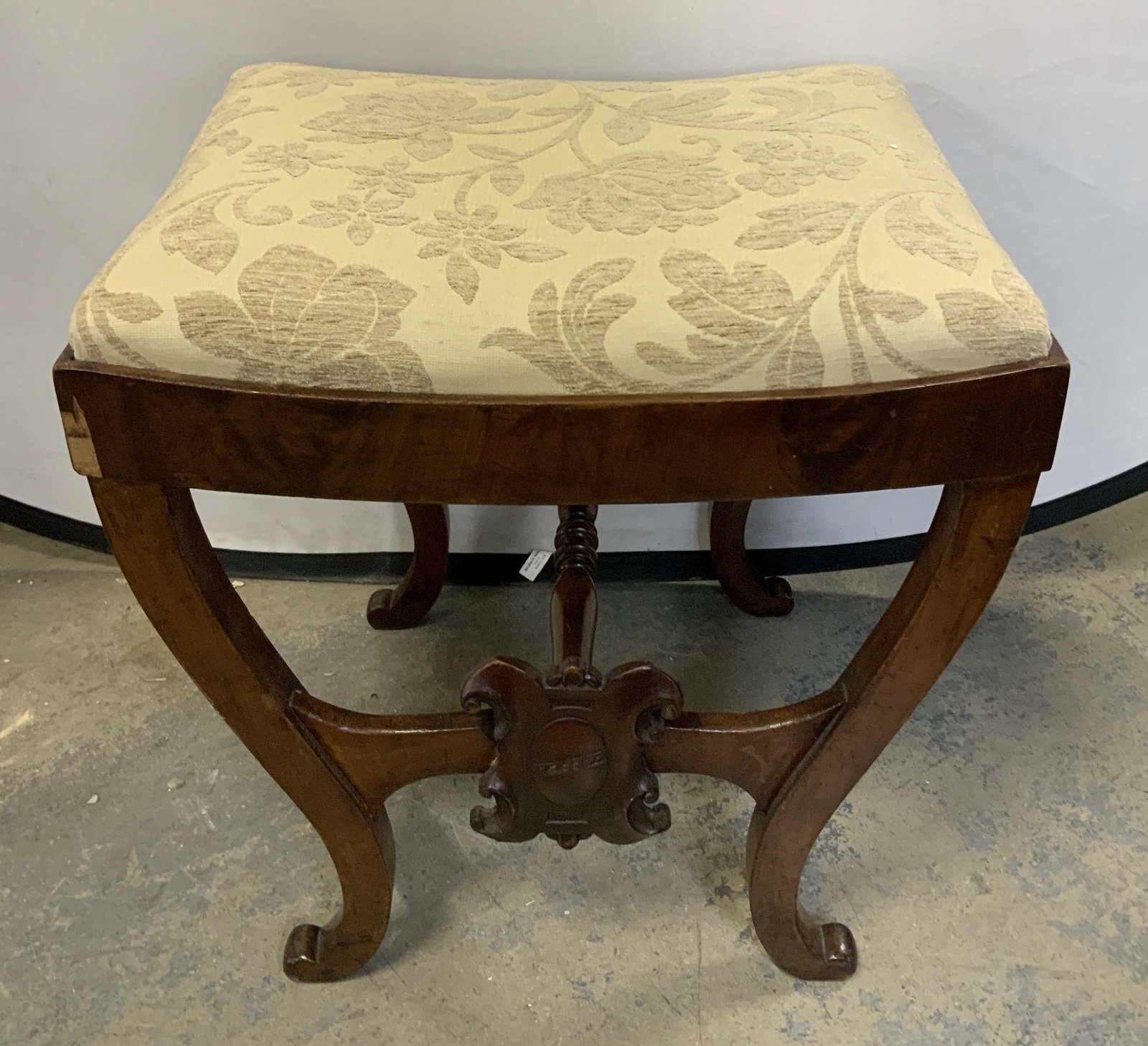 Antique Empire Style Carved Wood Stool: Antique, possible vintage. Features a rectangular cushioned seat with beige floral upholstery, curved saber style legs. Dark wood finish. Empire style. No visible signature or markings. Surface wear c