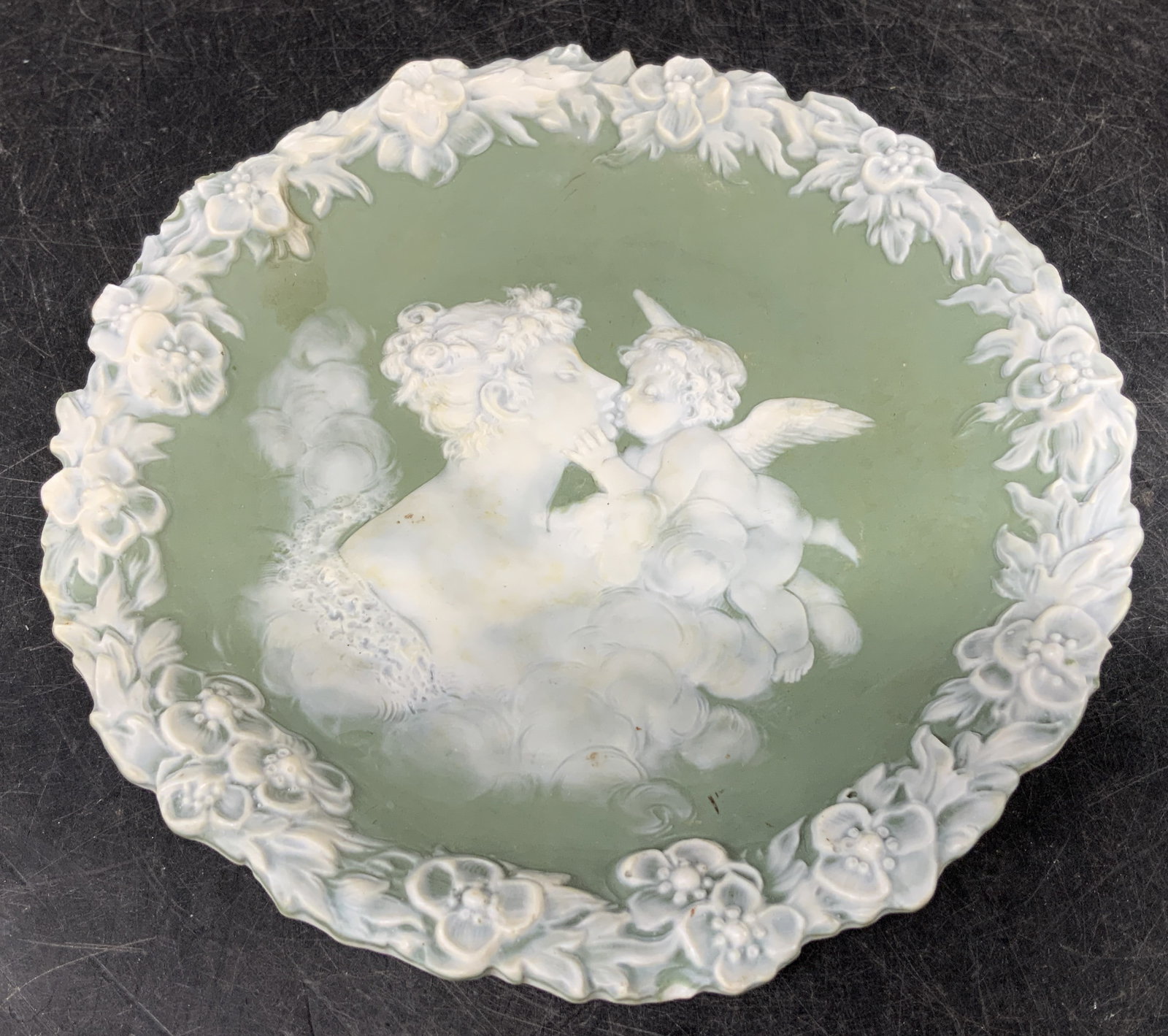Antique Kissing Cherub Jasperware Wall Plaque: Antique, possible vintage. Wall plaque depicting a cherub kissing a maiden. Intricate floral border. Green matte finish. Signed & marked on underside. Reads, 2701. Surface wear consistent to age, use 