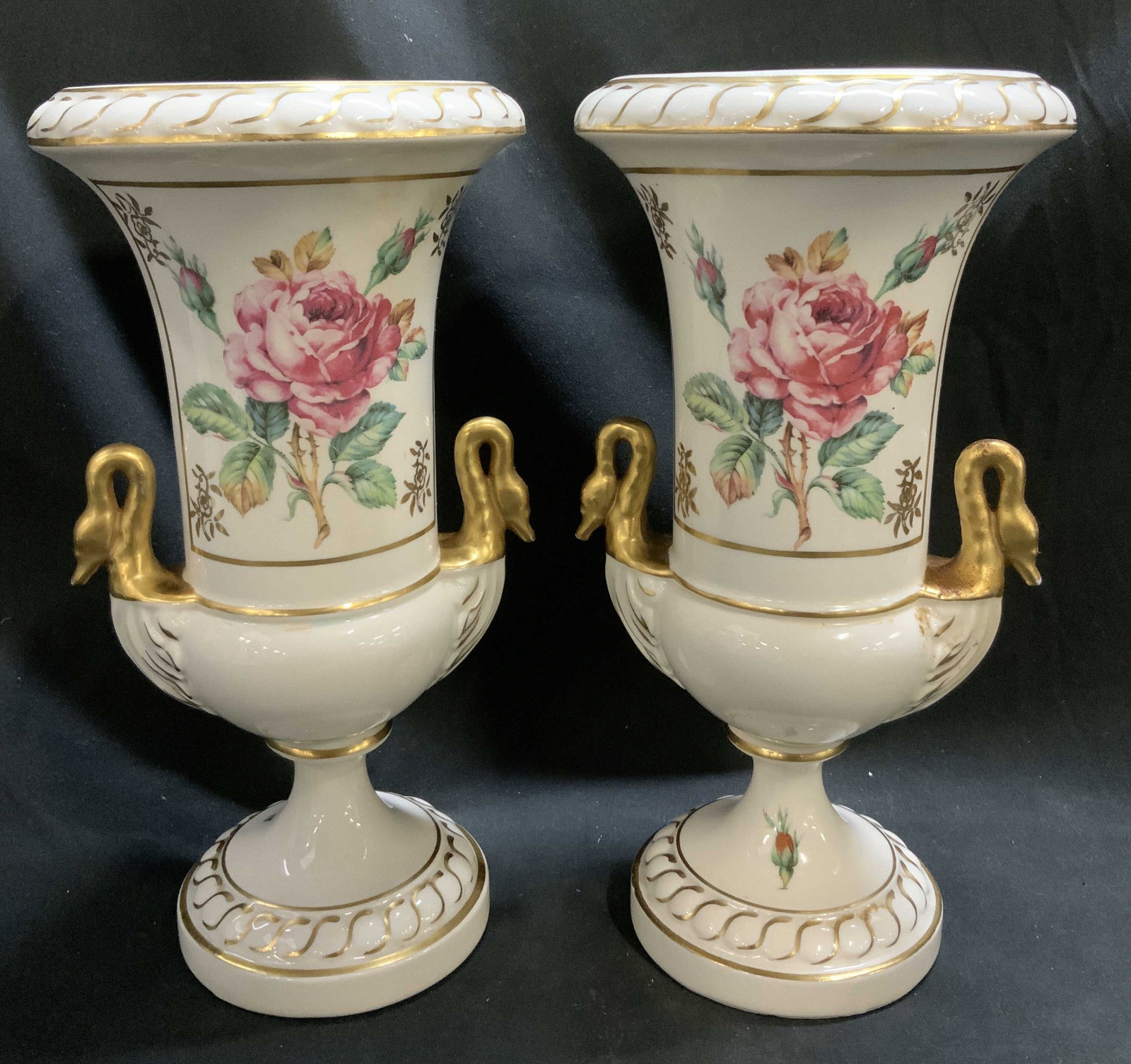 Pair Vtg Meissen Style Numbered Floral Trophy Vases: Each has imprinted number on underside. Lot includes, a pair of vintage white trophy vases featuring pink floral motifs in center & gilt swan handles. Round base. Meissen style. Surface wear consisten