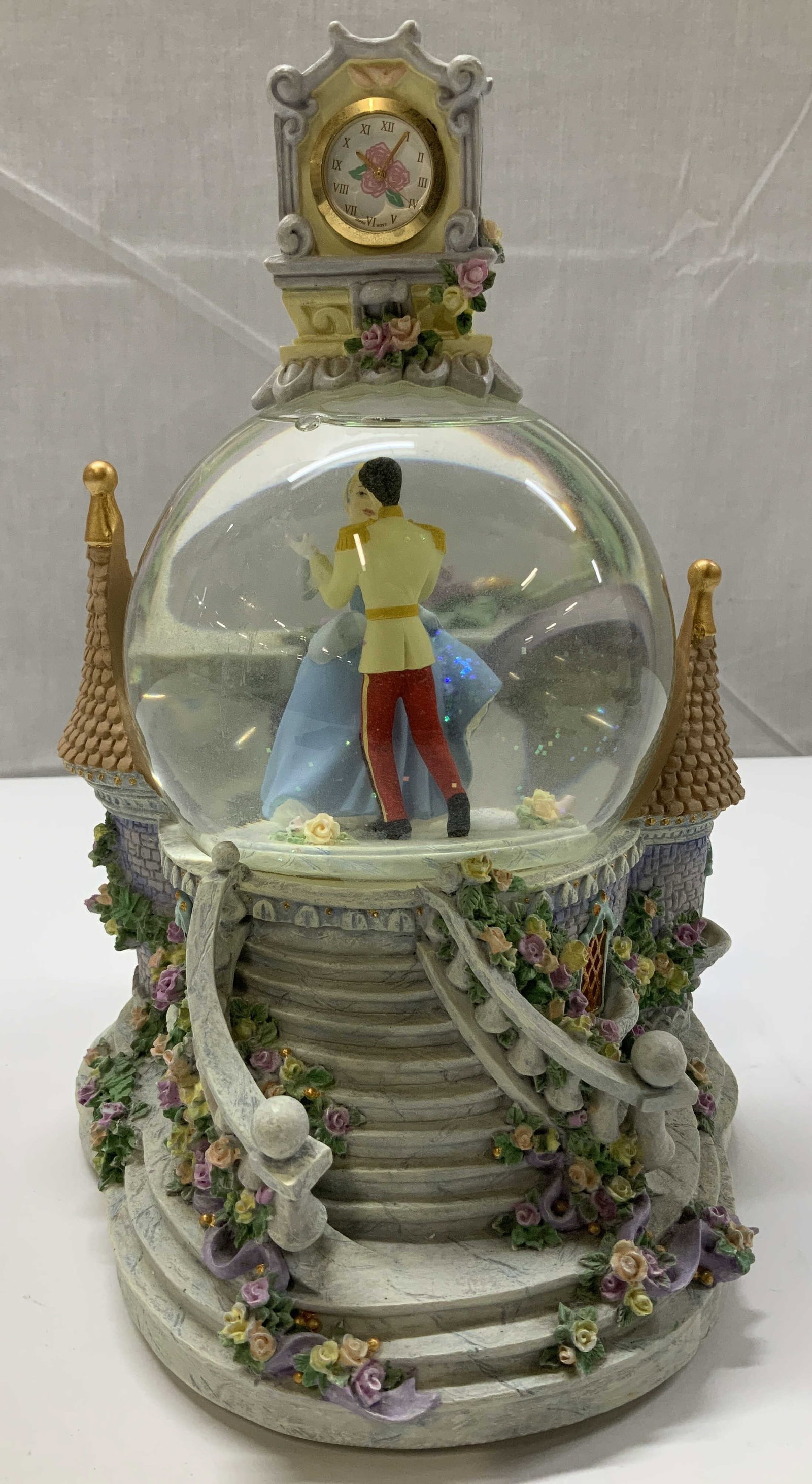 Disney Cinderella & Charming Musical Snow Globe: Disney Cinderella & Prince Charming musical snow globe. Top features a clock. Plays, So This is Love. Intricate detailing. Resin material. Signed & marked on underside. Reads, DISNEY JAPAN. Surface we