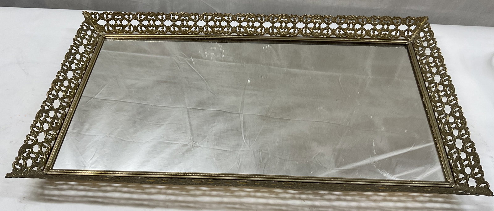 Vintage Gold Toned Mirrored Vanity Tray: Vintage gold toned mirrored vanity tray. Rectangular shape. Ornate scroll motif border. Gold toned. Measures approx 12 x 22 inches. Surface wear consistent with exposure. Vanity tray, tray, mirrored v