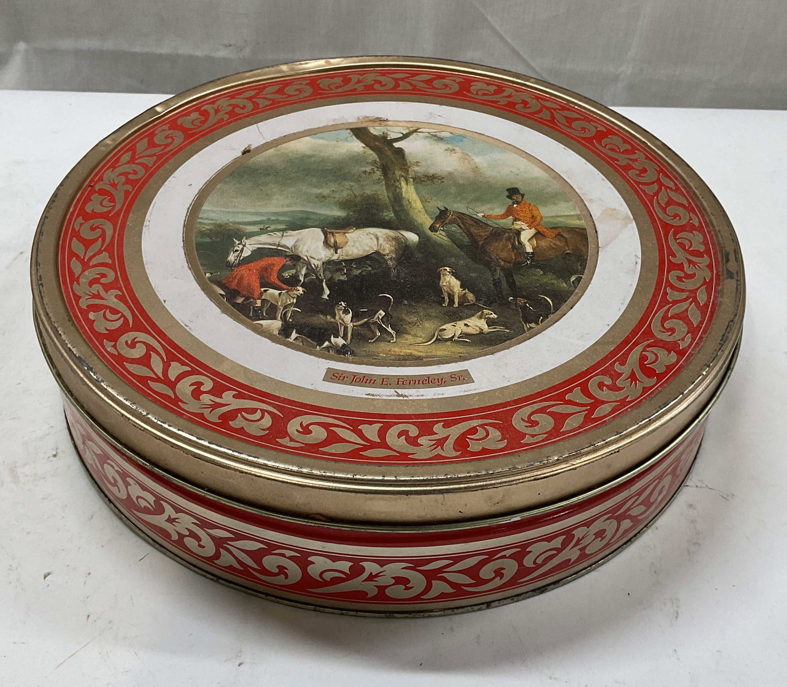 Vtg Hunting Scene Ferneley Round Tin Box: Vintage decorative round biscuit tin box with Sir John. Ferneley Sr hunting scene motif. Red and gold tone scroll border. Measures approx. 12 x 3.25 inches. Some warping and scratching. Decorative tin