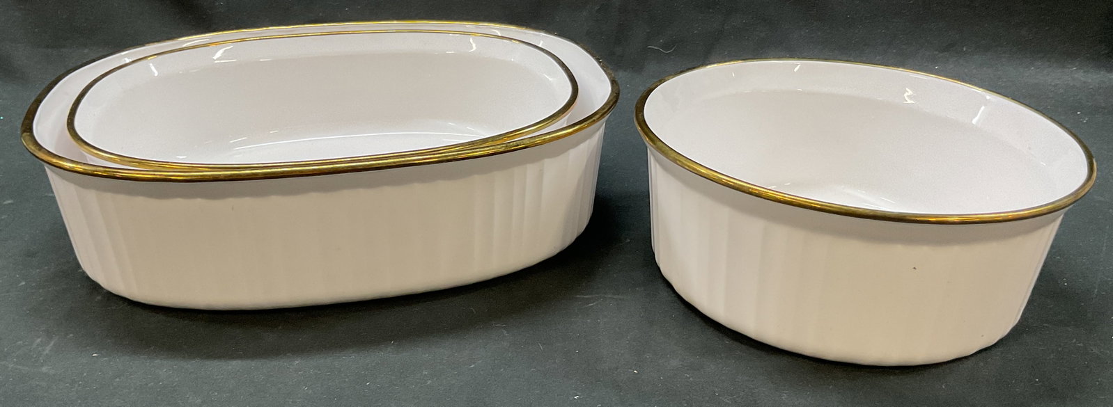 Set 3 CorningWare Ceramic Casserole Dishes USA: Set of 3 CorningWare ceramic casserole dishes. Made in USA. Marked on underside. Oval and circular shaped. Gilt rim. Ribbed surface. Largest measures approx 8.5 x 11 x 3 inches. Surface wear consisten
