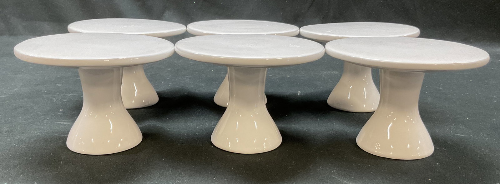 Set 6 White Ceramic Pedestal Cake Stands: Set of 6 white ceramic pedestal cake stands. Marked Earthenware on underside. Pedestal base with round tops. Measures ht approx 3 inches diam approx 3 inches. Surface wear consistent with exposure. Ca