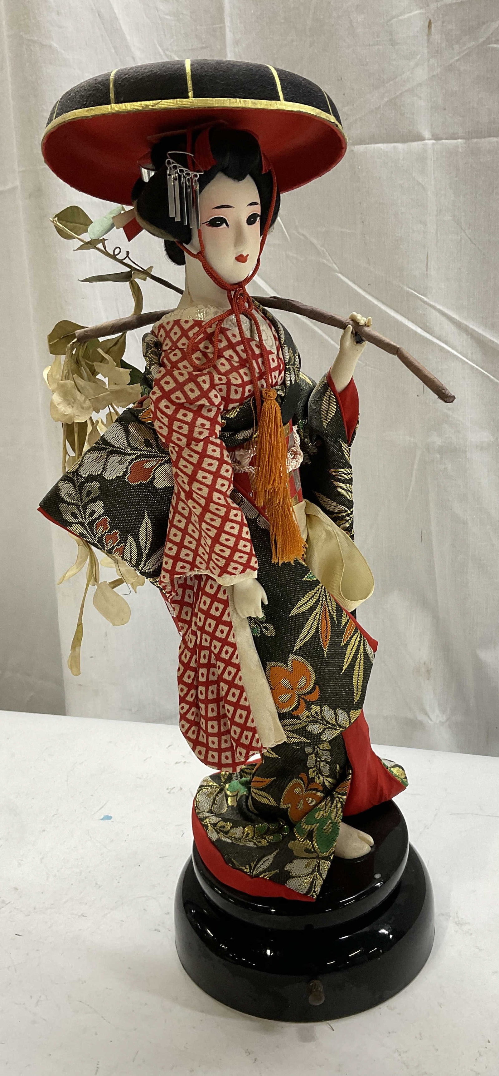 VTG Asian Mask-Face Doll on Rotating Musical Stand: Vintage Asian Mask-Face Doll on Rotating Musical Stand. Depicts a Woman in Traditional Attire Carrying a Branch Over her Shoulder. Stand Has Dial. Has Not Been Tested For Functionality. Condition Cons
