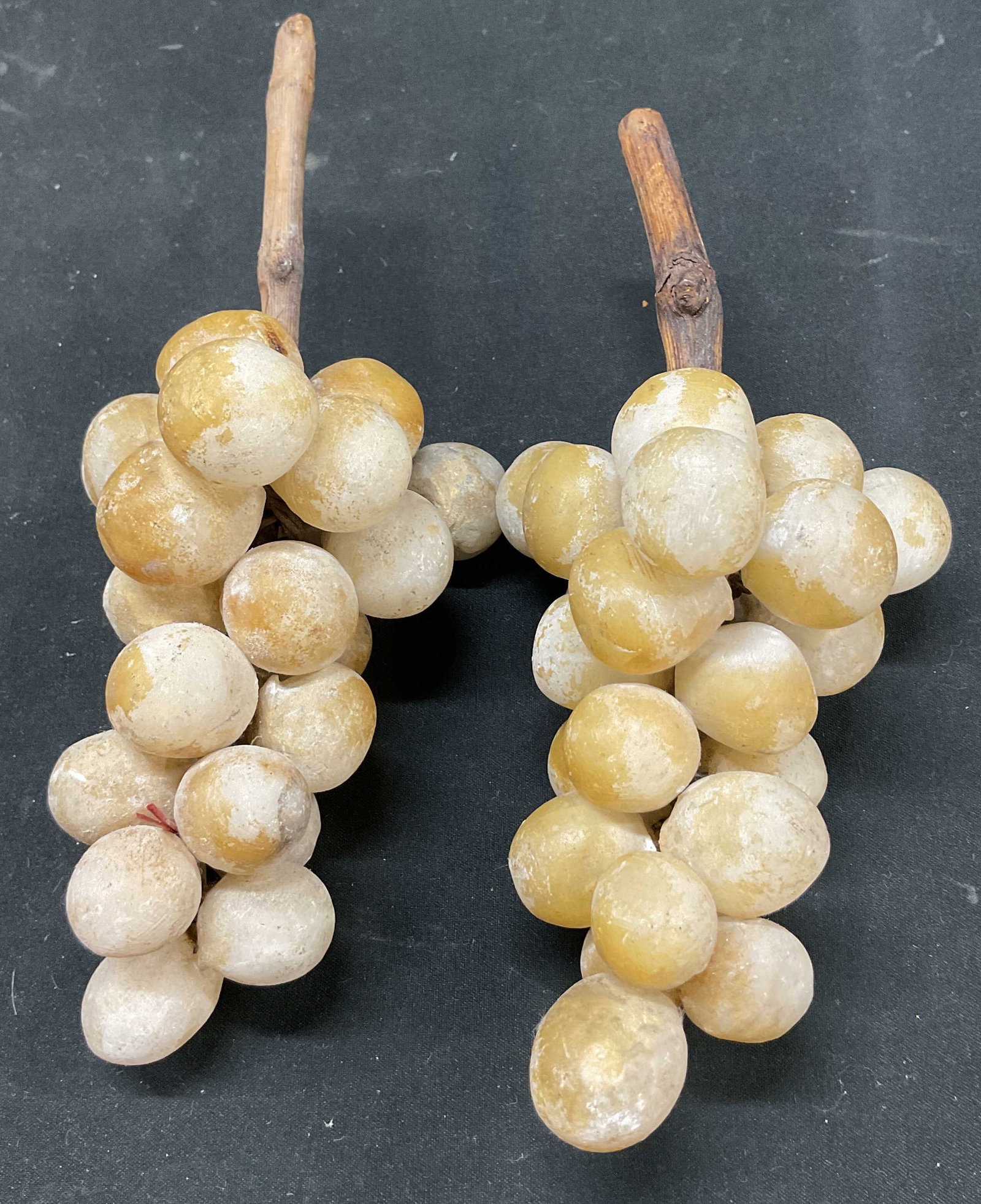 Pair Vintage Natural Stone Grape Clusters: Pair of vintage natural stone grape clusters. Wooden stems. Appears to be alabaster stone. White yellowish color. Measures approx 2.5 x 7 inches. Surface wear consistent with exposure. Grape clusters,