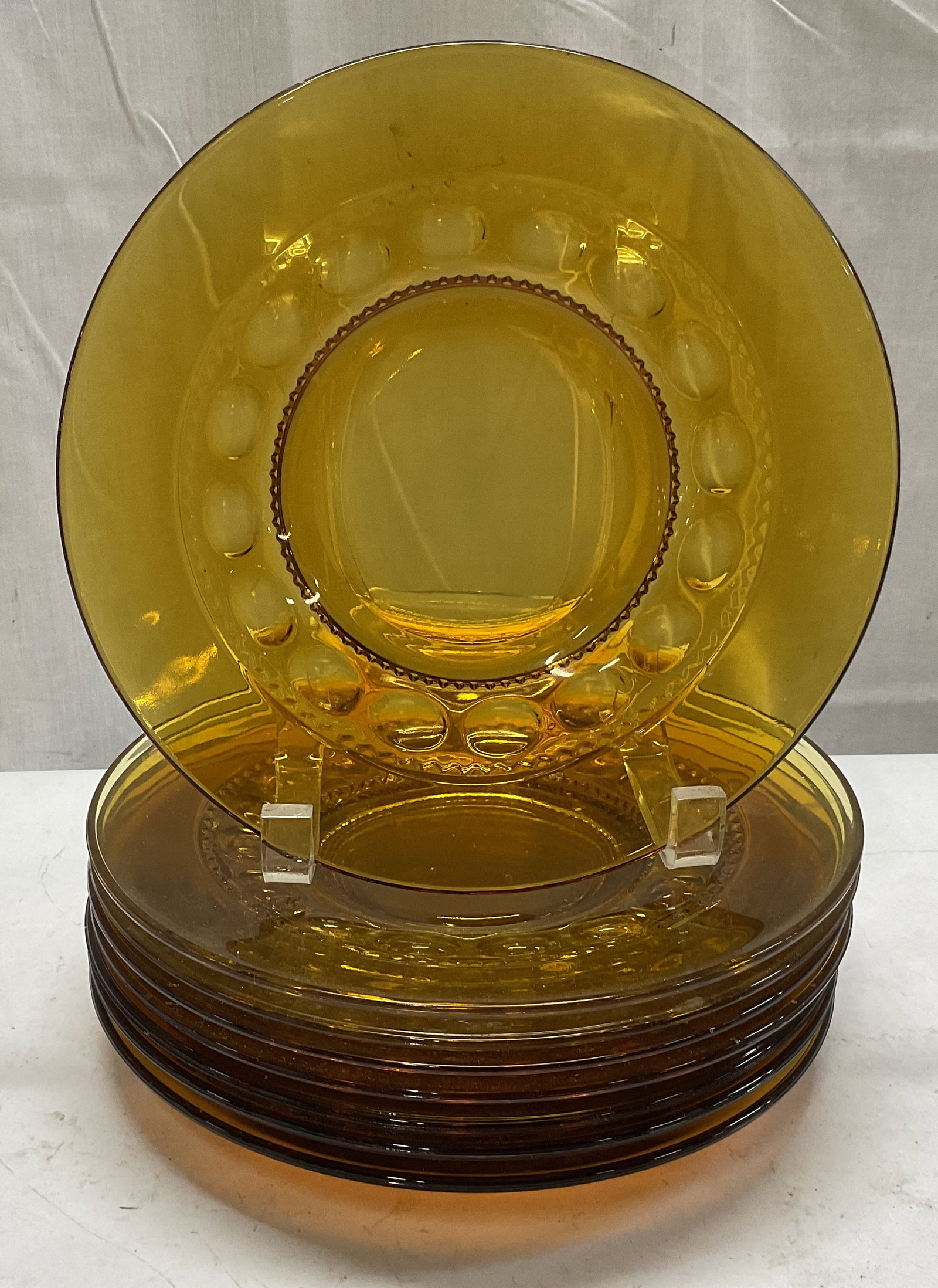 St 8 VTG Amber Glass Thumbprint Design Plates: Set of 8 Vintage Amber Glass Thumbprint Design Plates. Some Scratching Consistent with Exposure. Varying Yellows and Orange. Measures app 1in H x 8.25in Diameter. Vintage Glassware, Vintage Glass Plat