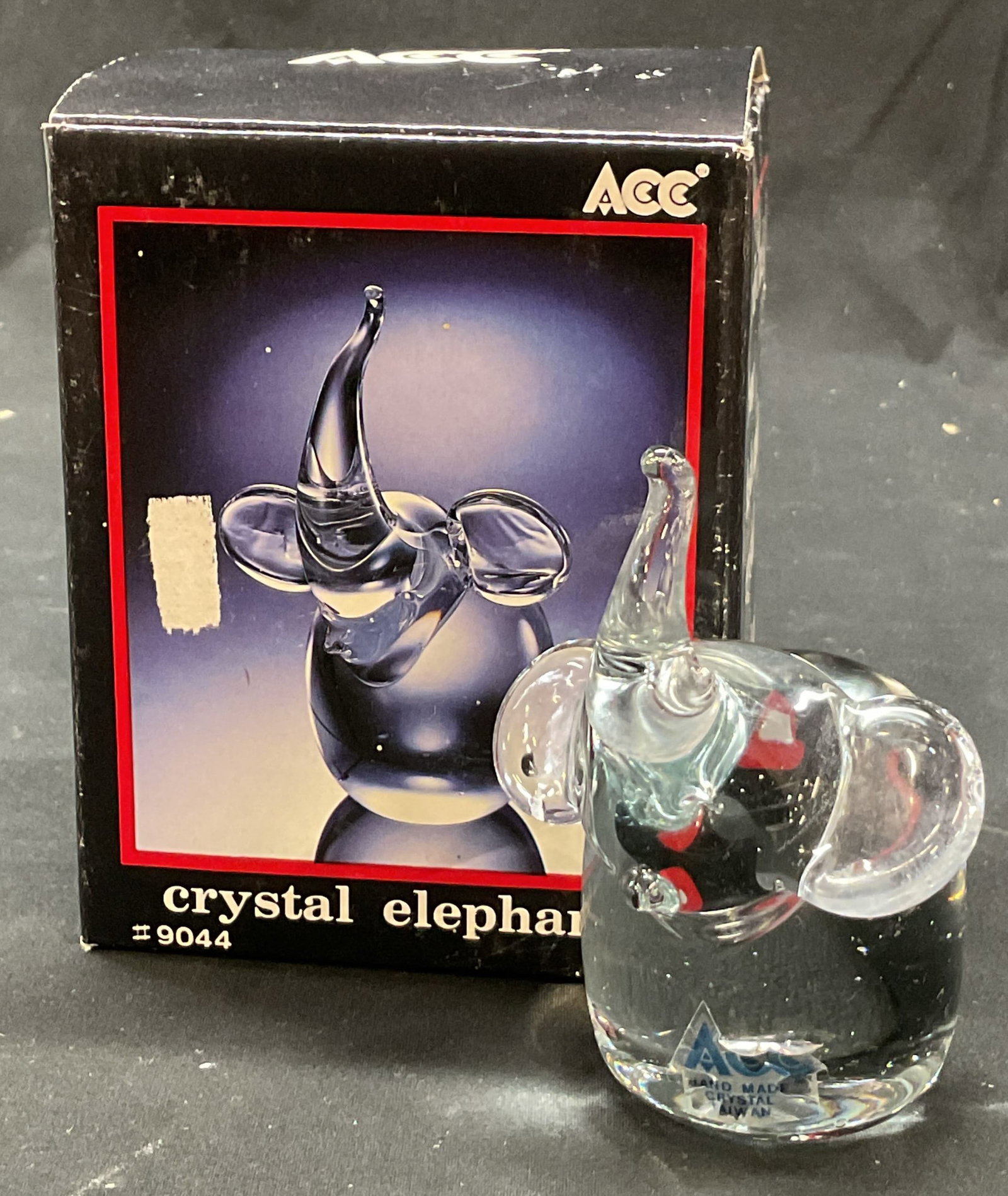ACC Crystal Elephant Figure W Org Box: ACC crystal elephant figure. Comes in original box. Marked on surface with sticker. Detailed features. Elephant sitting figure. Measures ht approx 4 inches base diam approx 2 inches. Some scratching. 