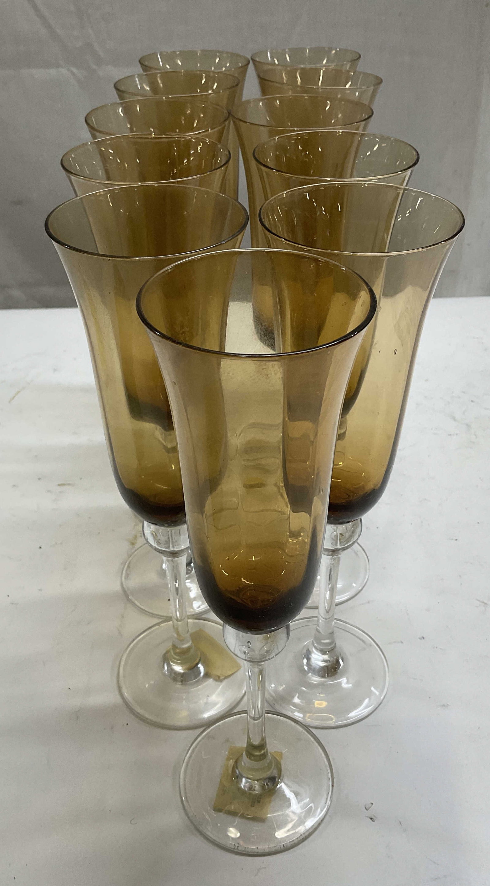 St 11 Kanco Corp USA Amber Glass Champagne Flutes: Set of 11 Kanco Corp USA Bell-Shaped Amber Glass Champagne Flutes. Clear Glass Stems with Glass Bubble. Hand Crafted. Some Wear and Residue Present. Measures app 9.75in H x 2.75in Diameter. Bell-Shape