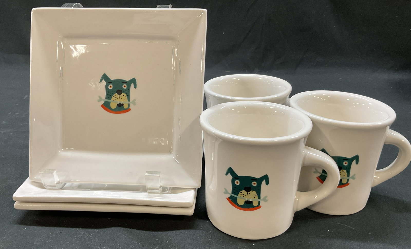 Set 6 Fishs Eddy Jessie Hartland Tableware: 6 piece Fishs Eddy Jessie Hartland ceramic tableware set. Marked on underside, reads Jessie Hartland For Fishs Eddy. Includes 3 mugs and 3 plates. Features cartoon dog with a bone in its mouth in vary
