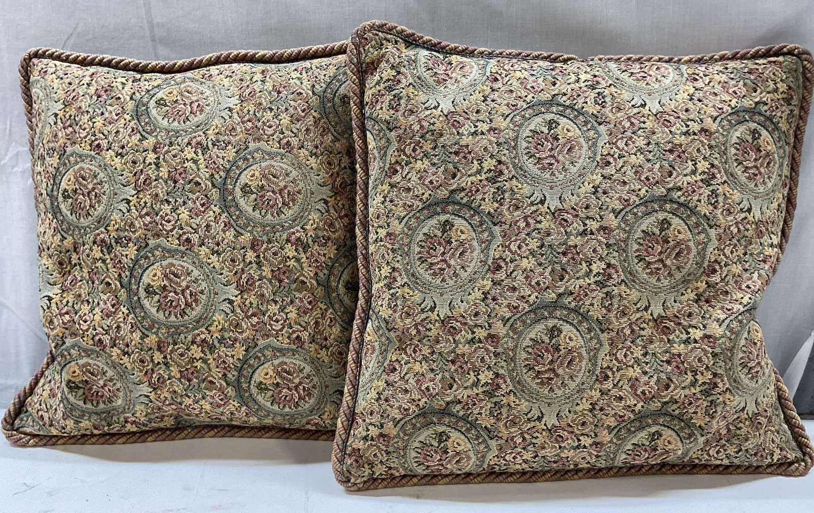 Pair Floral Medallion Decorative Throw Pillows: Pair of floral medallion decorative throw pillows. Fabric and velvet. Braided trim. Floral medallion motifs in varying colors. Measures approx 16 x 16 inches. Surface wear consistent with exposure. Th