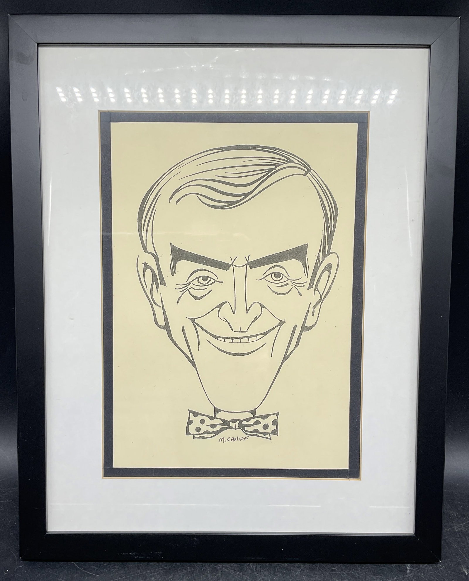 After Milton Caniff Caricature Lithograph: Framed and matted lithograph. After Milton Caniff. Caricature of a man wearing bow tie. Black frame. Not examined out of frame. Frame measures approx. 15.25 x 12.25 inches. Some wear consistent with e