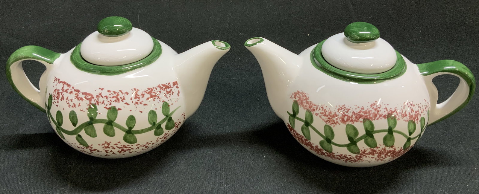 Pair Hand Painted Ceramic Teapots: Lot includes, a pair of ceramic teapots featuring hand painted leaf like motifs. Red & green. White body. Surface wear consistent to age, use & exposure. Measurements: length to handle 5.7in x width 3