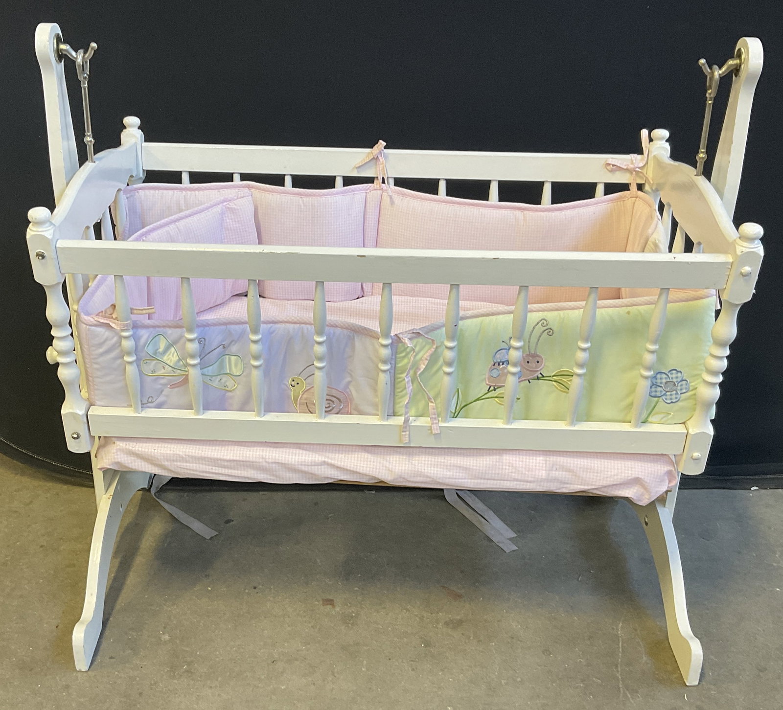 White Wooden Rocking Doll Cradle: Painted White Wooden Rocking Doll Cradle. Turned-Wood Spindles. Kids Line Pink & White Checkered Liner with Dragonflies, Snails, Ladybugs, and Flowers. Condition consistent with exposure. Bottom