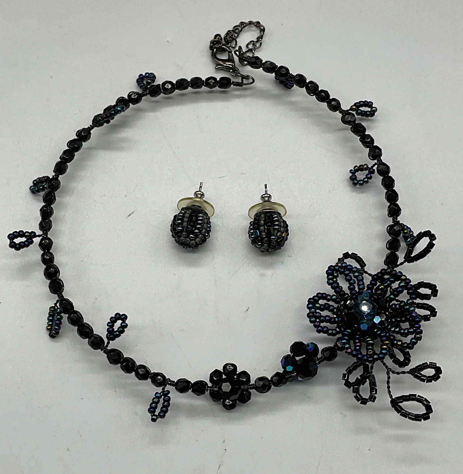 Set 2 Black Blue Beaded Necklace & Earrings: Set of 2 pieces black and blue beaded stud earrings and floral necklace. Necklace drop length measures approx. 5.5 inches. Earrings measures approx. .5 inches wide. Some scratching. Includes a box. Je