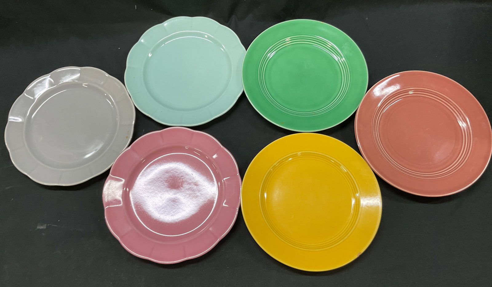 Lot 7 Vintage Colorful Ceramic Plates: Lot of 7 vintage colorful ceramic plates. No visible markings. Round plates. Scalloped edges. Colors include yellow, blue, green, pink, two red, and grey. Glossy finish. Measures approx 9 inches in di