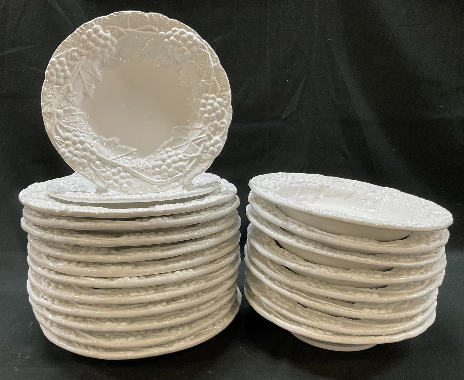Set 21 Vtg Ceramic Majolica Grapevine Tblw Italy: 21 piece vintage white ceramic majolica grapevine tableware set. Marked made in Italy on underside. Includes 8 bowls, 11 dinner plates, and 2 lunch plates. Scalloped edge. Embossed grapevine motifs. G