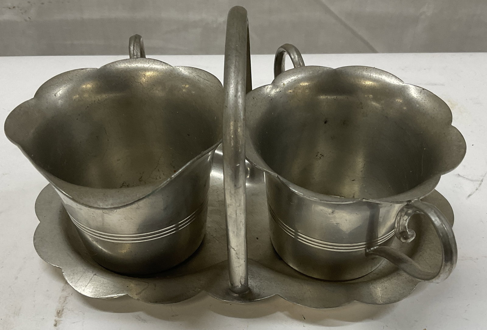 VTG Pewter Creamer & Sugar on Caddy: Vintage Pewter Creamer & Sugar on Caddy. Bottom Reads Pewter 688. Scalloped Trim. Measures app 3.5in H x 7in L. Some Scratching and Wear to Metal. Vintage Creamer and Sugar Set, Pewter Creamer and Sug