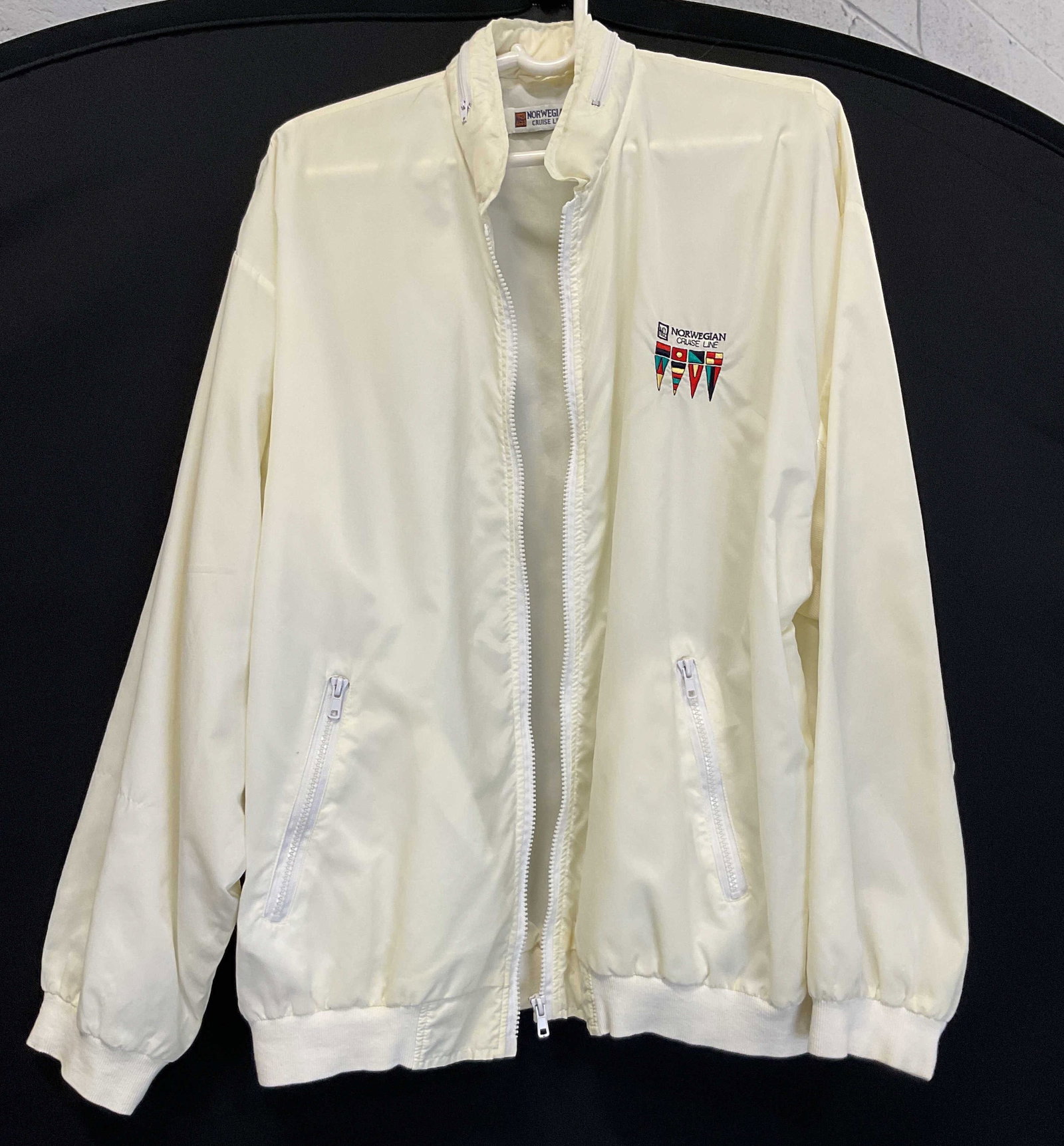 Norwegian Cruise Line White Windbreaker: Norwegian Cruise Line white windbreaker. Collared and zippered. Zippered pockets. Embroidered Norwegian Cruise Line logo in varying colors. Measures approx 19 inches across chest. Some blemishes.