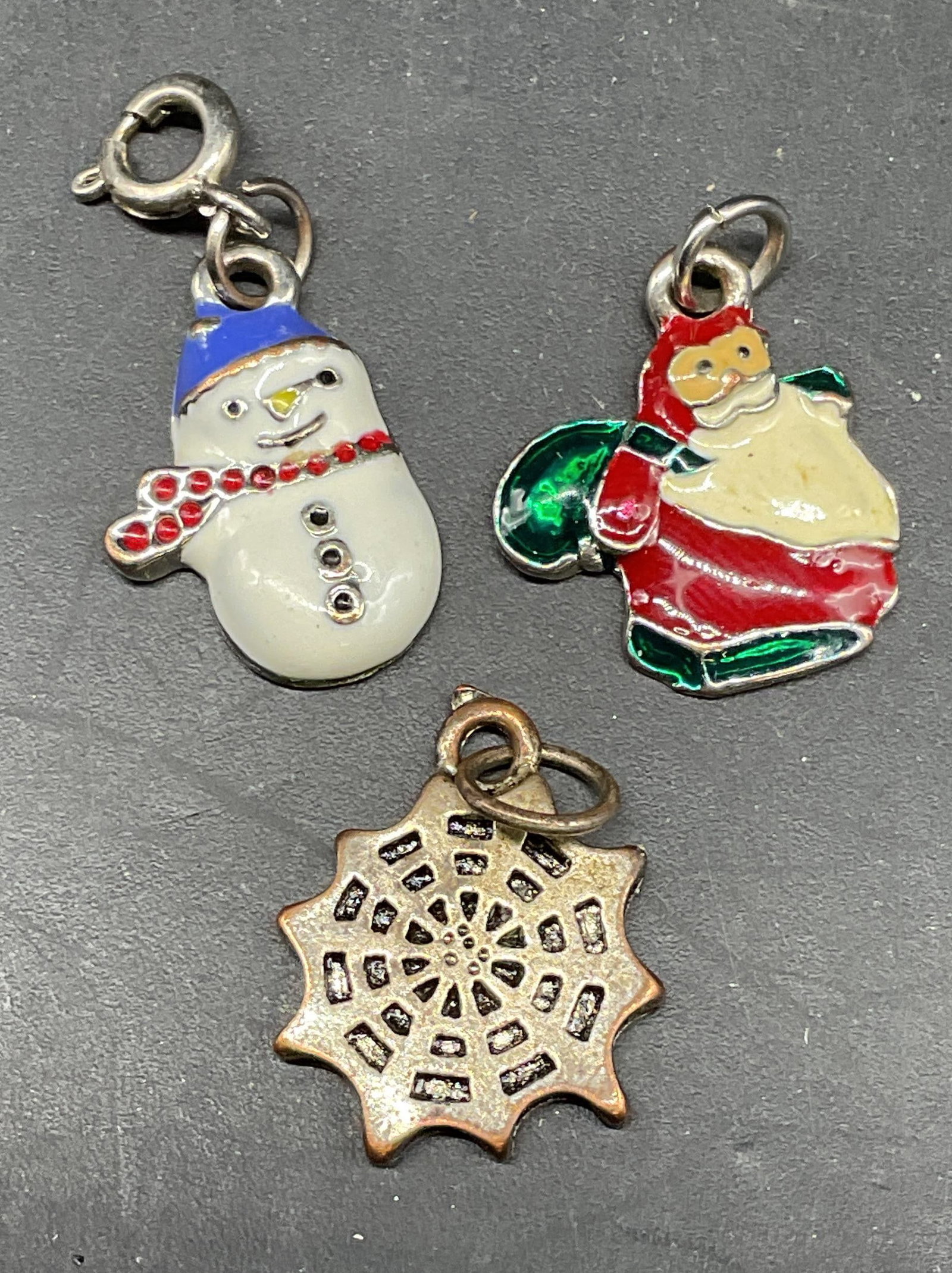 Lot 3 Santa, Snowman, Spiderweb Charms: Lot of 3 charms. Enameled Santa and snowman motif charms. Silver tone spiderweb charm. Santa charm measures approx. 5/8 inches long. Some scratching. Jewelry, estate jewelry, costume jewelry, cocktail