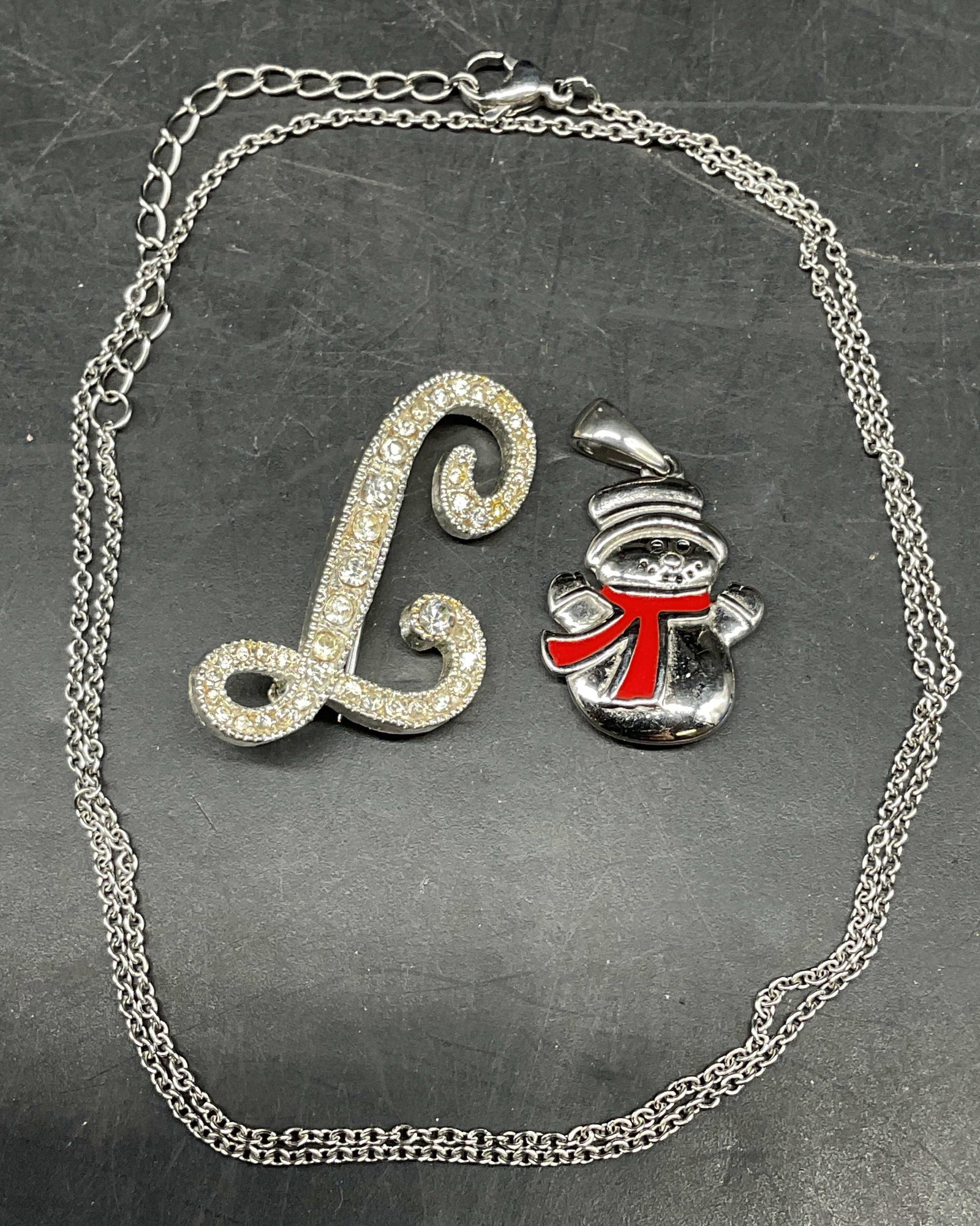 Lot 3 HMK Snowman Pendant, L Brooch +: Lot of 3 jewelry pieces. Signed HMK stainless steel enameled snowman pendant, measures approx. 1 inch long. Silver tone crystal initial L brooch, measures approx. 1.25 x .75 inches. Silver tone chain 