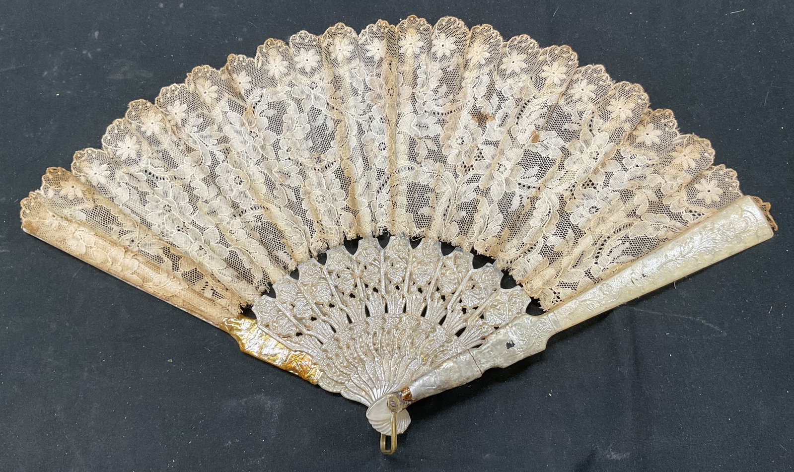 Vintage Lace Folding Hand Fan: Vintage lace folding hand fan. Ornate lace material with floral motifs. Scalloped trim. Floral and scroll motifs on panels. Measures approx 9.5 x 14 inches. Blemishes and wear to surface. Property of 