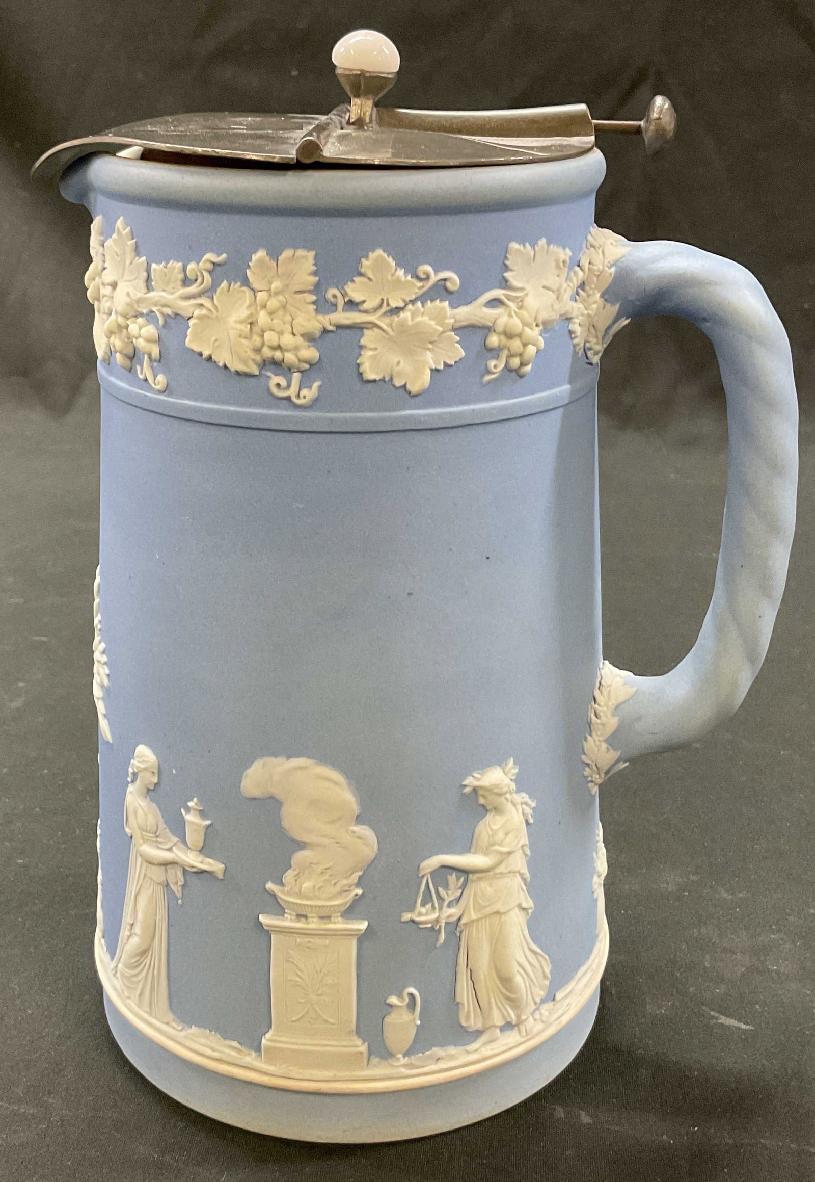 Wedgwood Blue Jasperware Pitcher England: Wedgwood blue Jasperware pitcher. Marked on underside, reads Wedgwood England. Ribbed and curved handle. Bulbous body and curved spout. White bas relief neoclassical motifs. Figural, grapevine, and sc