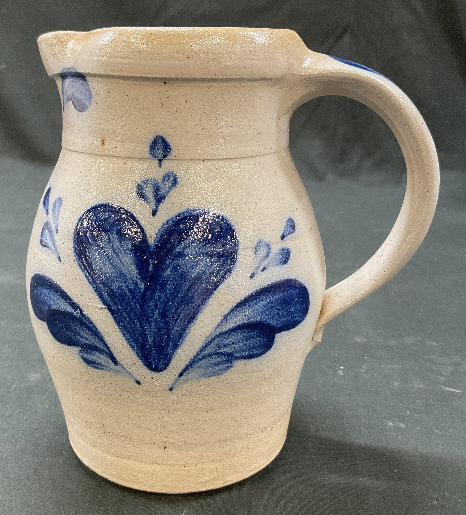 1990 Rowe Pottery Works Stoneware Pitcher USA: 1990 Rowe Pottery Works stoneware pitcher. Marked on backside, reads Handmade Rowe Pottery Works Cambridge, Wis 1990. Curved handle and spout. Salt glaze finish. Hand painted blue heart and leaf motif