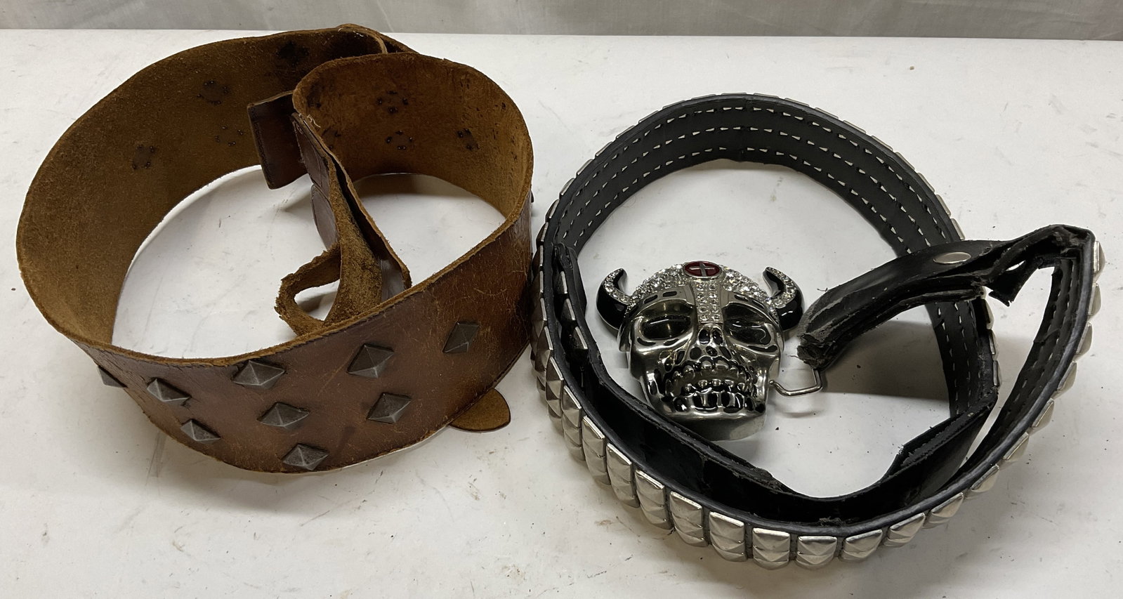 Lt 2 Studded Leather Style Belts: 2 Studded Leather Style Belts. Includes Black Leather Style with Horned Skull Buckle with Rhinestone Accents Size 34 and Brown Leather Style Belt with Studs. Surface Wear Including Fraying and Peeling