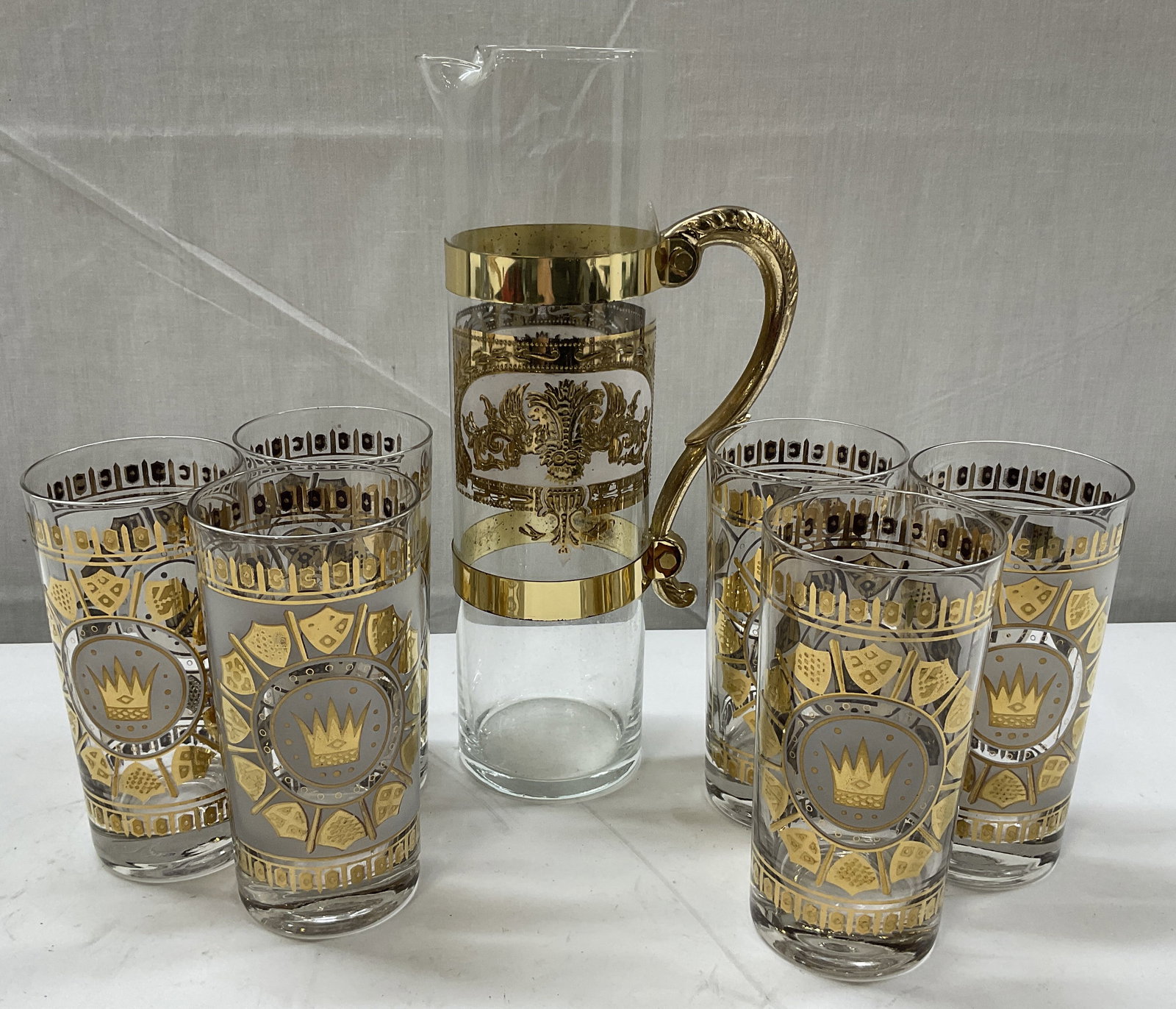 Lt 7 VTG Georges Briard Style Crown Gilt Pitcher+: 7 Vintage Georges Briard Style Crown and Shield Gilt Pitcher and Glasses. Pitcher has Gold Toned Metal Handle and Trim. Some Fading and Peeling. Measures app 11in H x 3.25in Diam. Vintage Glassware, G