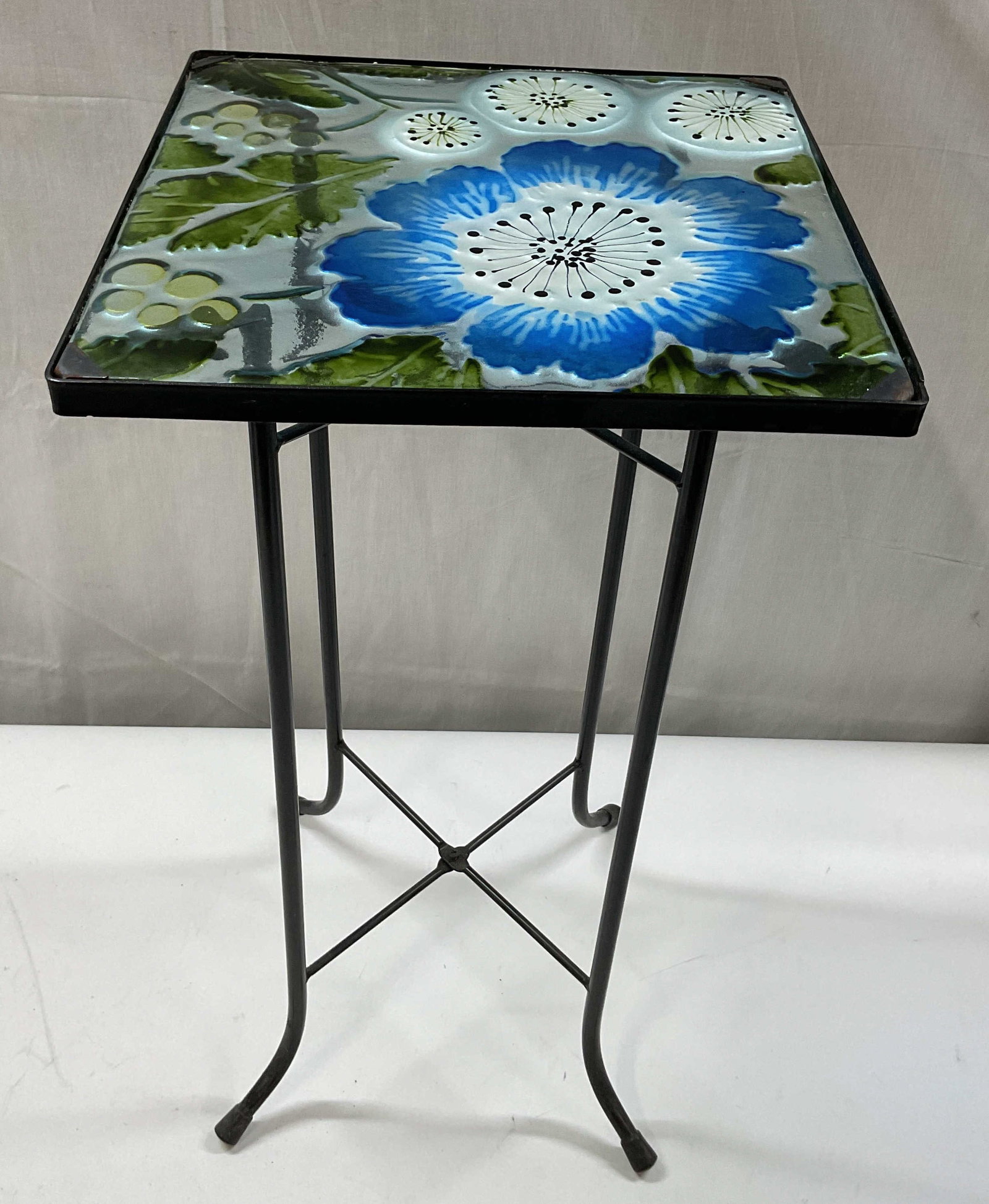 Gifted Living Poppy Flower Glass Patio Side Table: Gifted Living Poppy flower glass top patio side table. Square glass top. Painted embossed poppy flower and leaf motifs in blue, white, and green. Black metal curved legs. Measures approx 11 x 11 x 21 