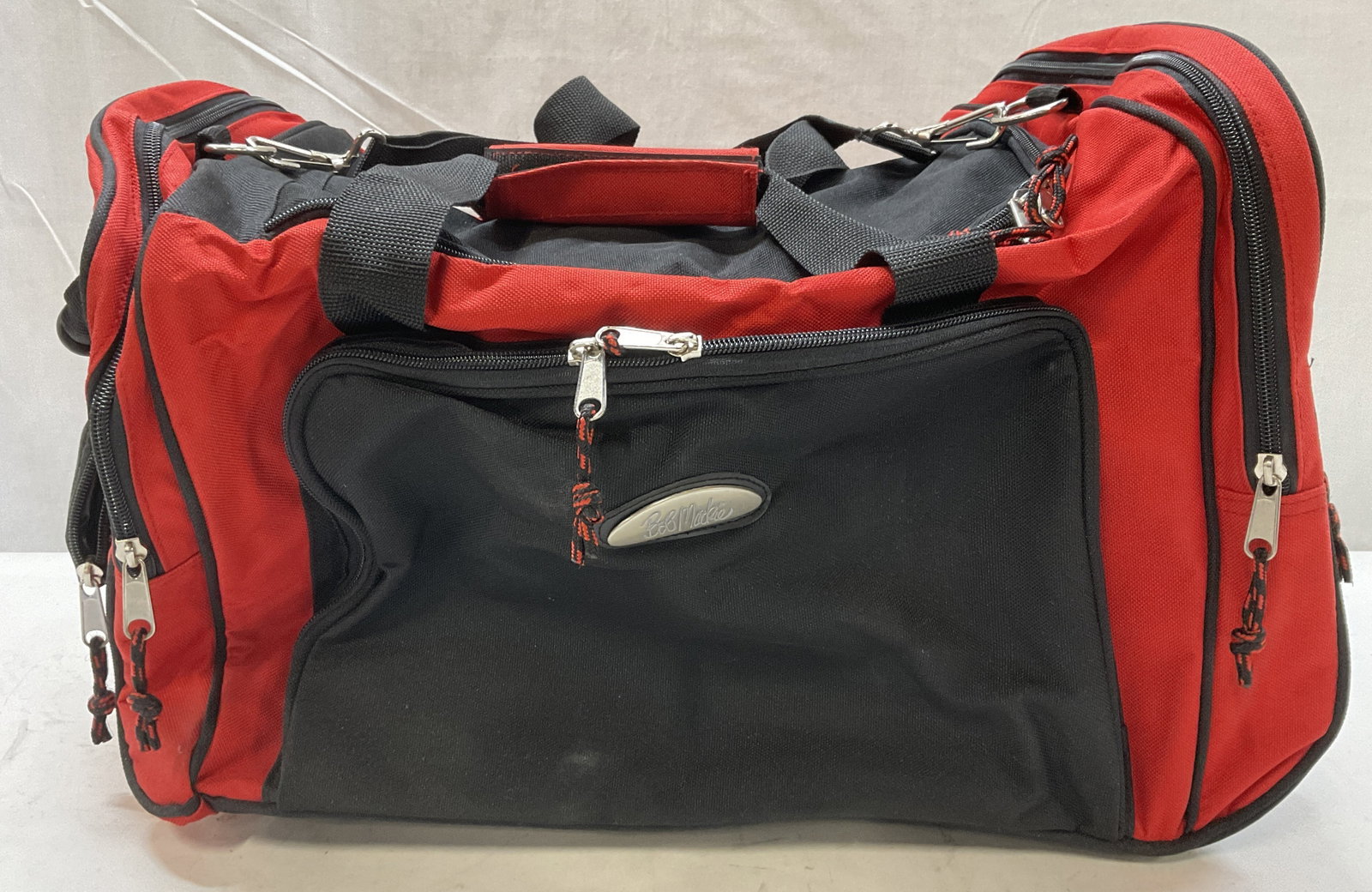 Bob Mackie Red and Black Duffel Bag on Wheels: Bob Mackie Red and Black Canvas Duffel Bag on Wheels. Inner Tag reads Another Quality Product Premium Bag The Better Company. Damage to Hard Casing Inside. Measures app 14in H x 18in W. Bob Mackie, Re