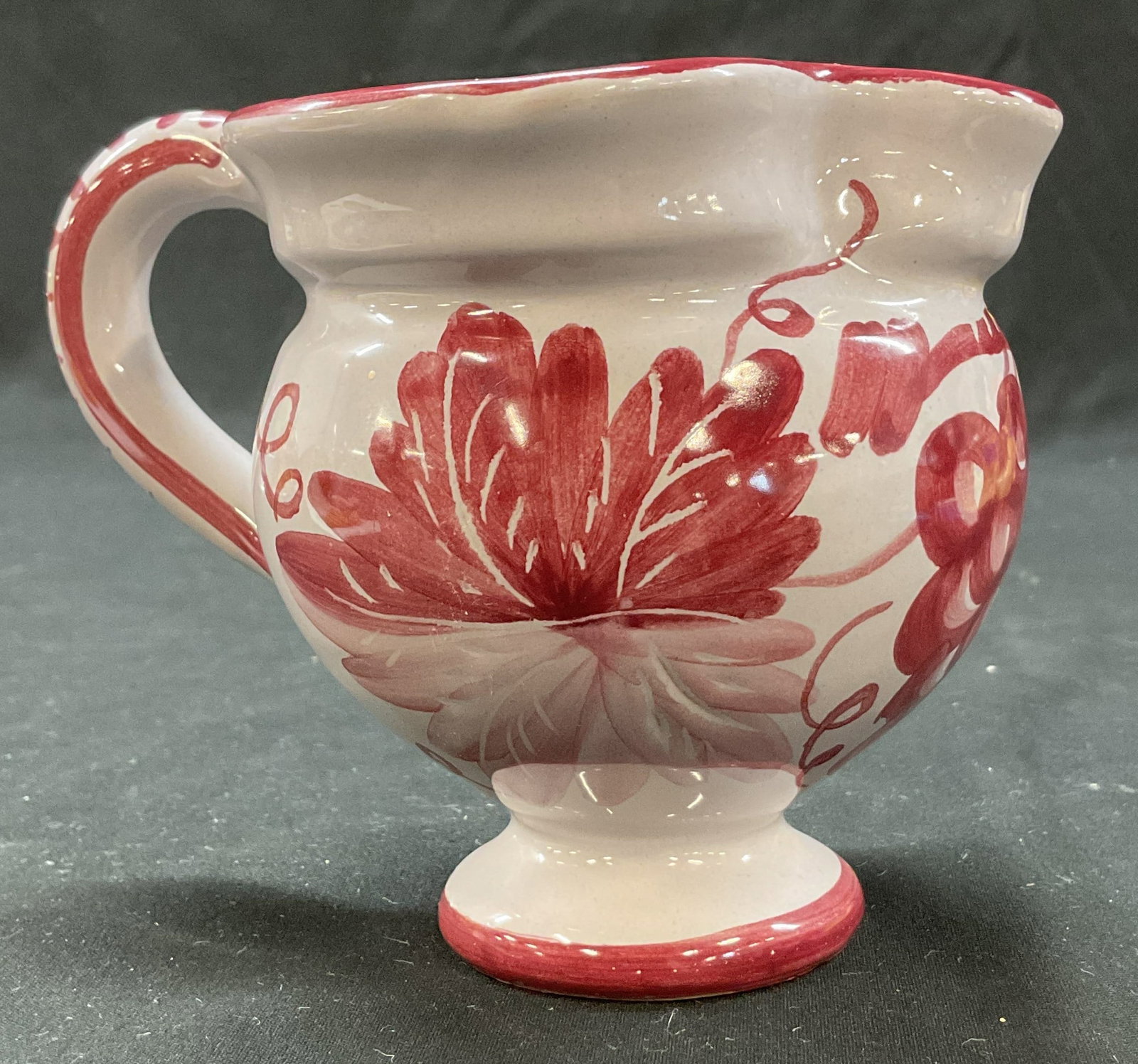 Vintage Hand Painted Ceramic Pitcher: Vintage hand painted ceramic pitcher. Signed on underside, reads illegibly. Short pedestal base. Round bulbous body. Curved handle. Hand painted floral, grape, and leaf motifs in pink. Measures approx