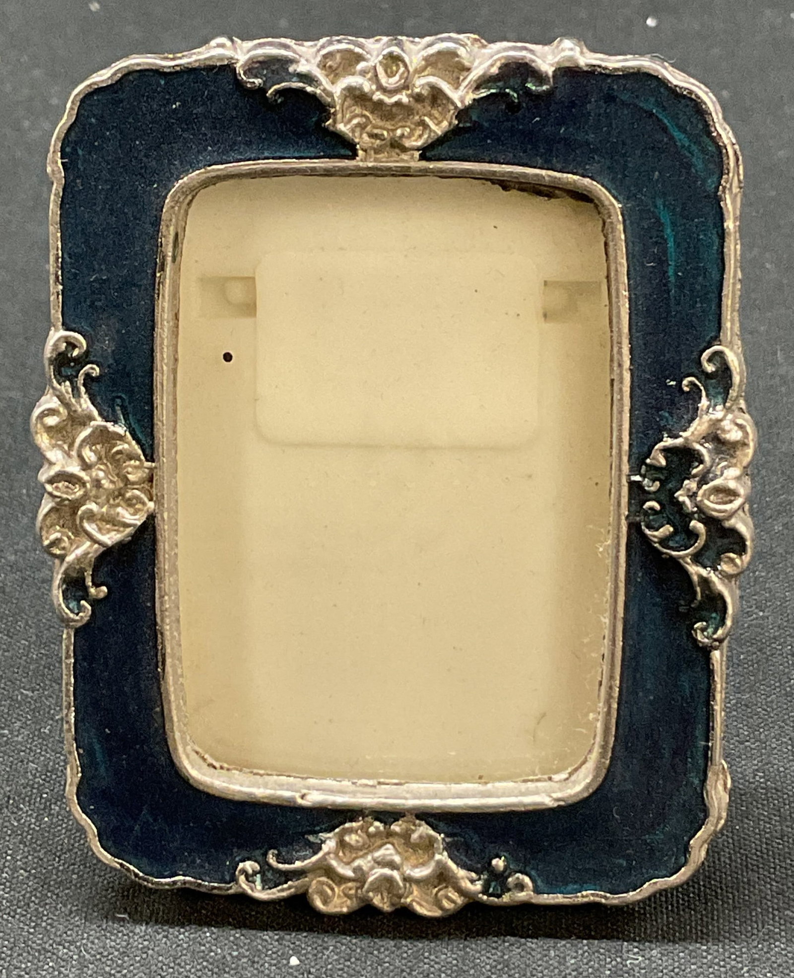 Davar Originals Silver Tnd Enamel Picture Frame: Davar Originals silver toned enameled picture frame. Marked Davar Originals. Silver toned floral motifs with blue enameled inlay. Scalloped edge. Measures approx 2 x 2.5 inches. Surface wear