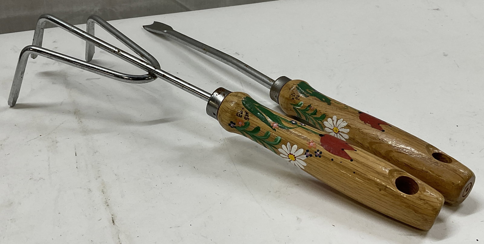 Lt2 SGND 93 Hand-Painted Folk Art Gardening Tools: 2 Vintage Artist Signed 1993 Hand-Painted Folk Art Gardening Tools. Reads Eb Sw and MS 93. Wooden Handles with Painted Tulip and Daisy Design. Includes a Garden Claw and a Weeder. Chipping to Paint