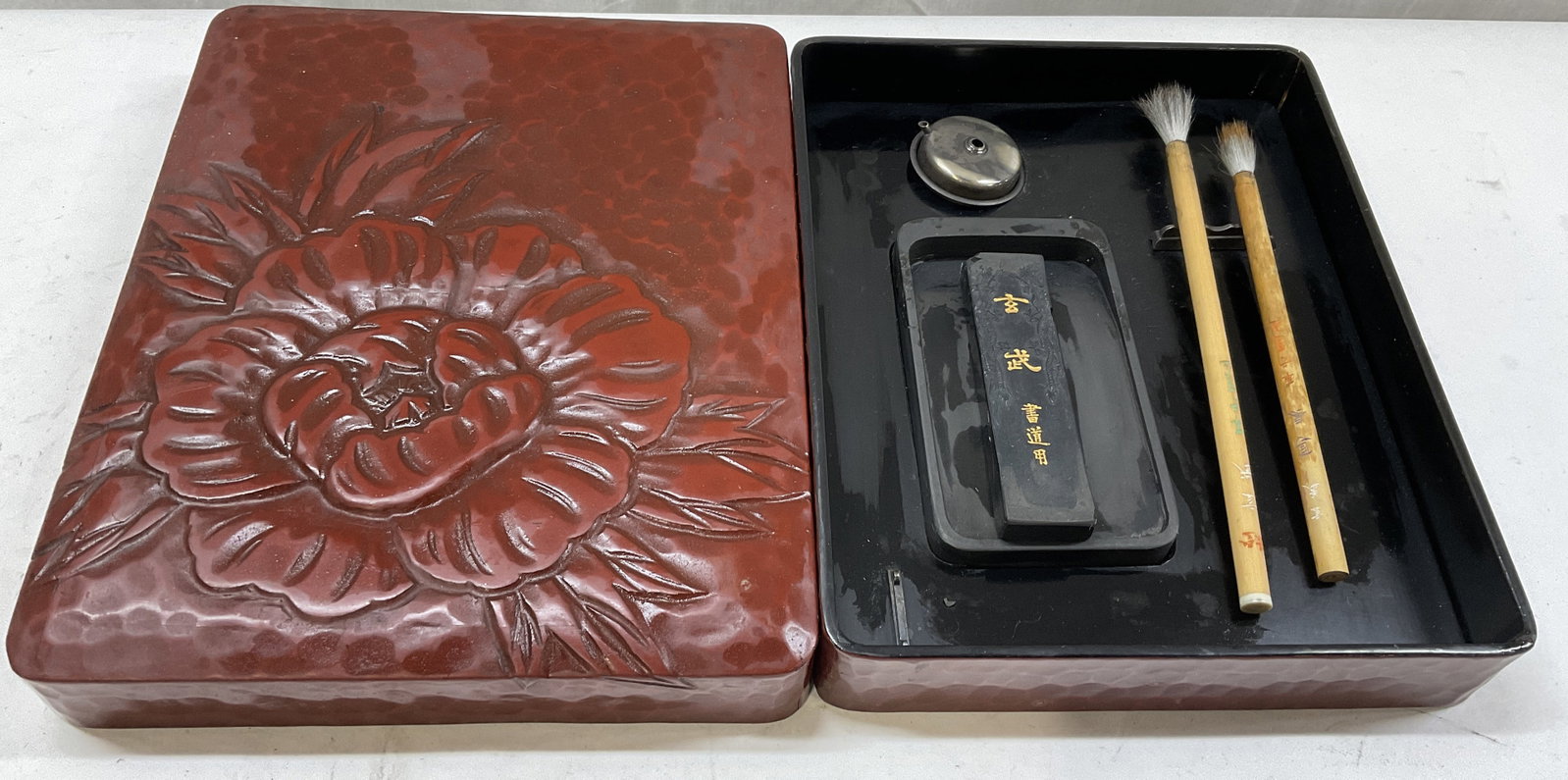 VTG Lacquer Sty Suzuri-Bako Calligraphy Box JPN: Vintage Red Lacquer Style Suzuri-Bako Calligraphy Box. Japan. Composite Material. Floral Design on Lid. Some Wear to Materials. Measures app 1.5in H x 9.5in L x 7.75in W. Vintage Calligraphy Box,