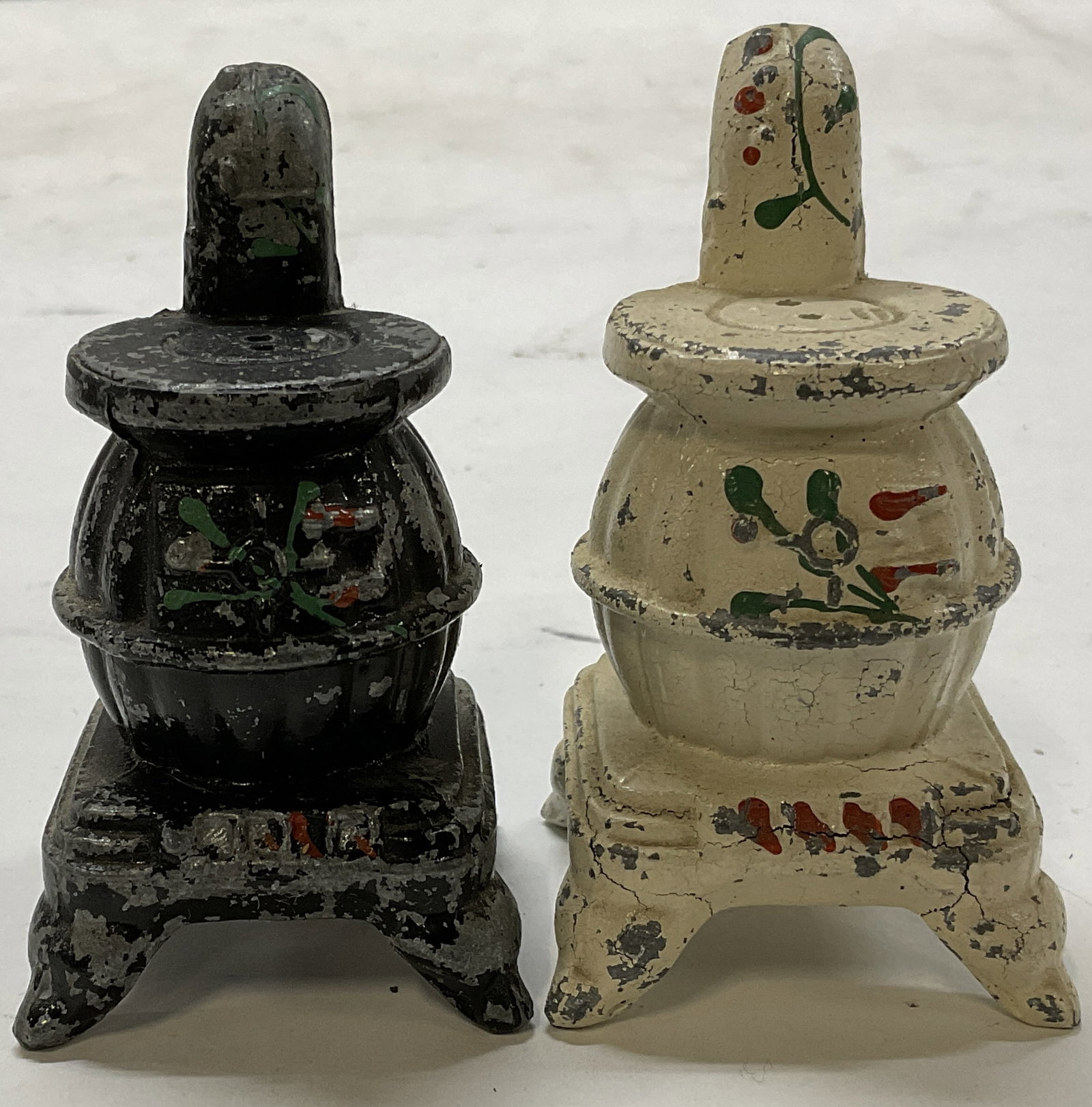 Lt2 Cast-Metal Potbelly Stove Shaped Shakers: 2 Vintage Cast-Metal Potbelly Stove Shaped Salt and Pepper Shakers. Hand-Painted Floral Pattern. Cork Stoppers. Some Cracks and Paint Chipping. Measures app 3in H x 1.5in W. Vintage Salt and Pepper