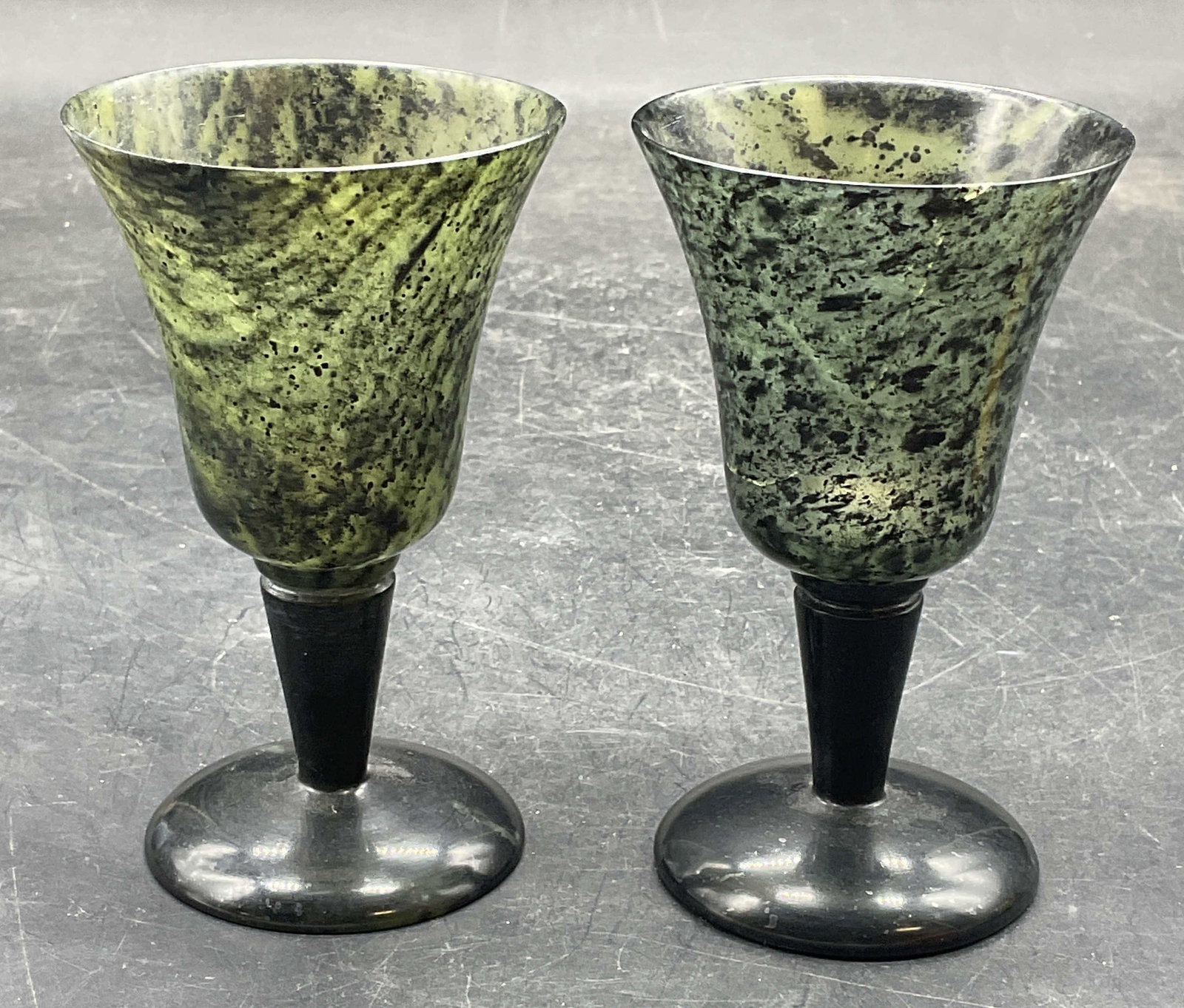 Pair Carved Green Stone Harmony Serenity Goblets: Pair of Asian carved green stone harmony & serenity goblets. Measures approx. 2.25 x 4 inches. Some scratching. Hairline and small chips to one goblet. Green stone cup, green stone goblet,