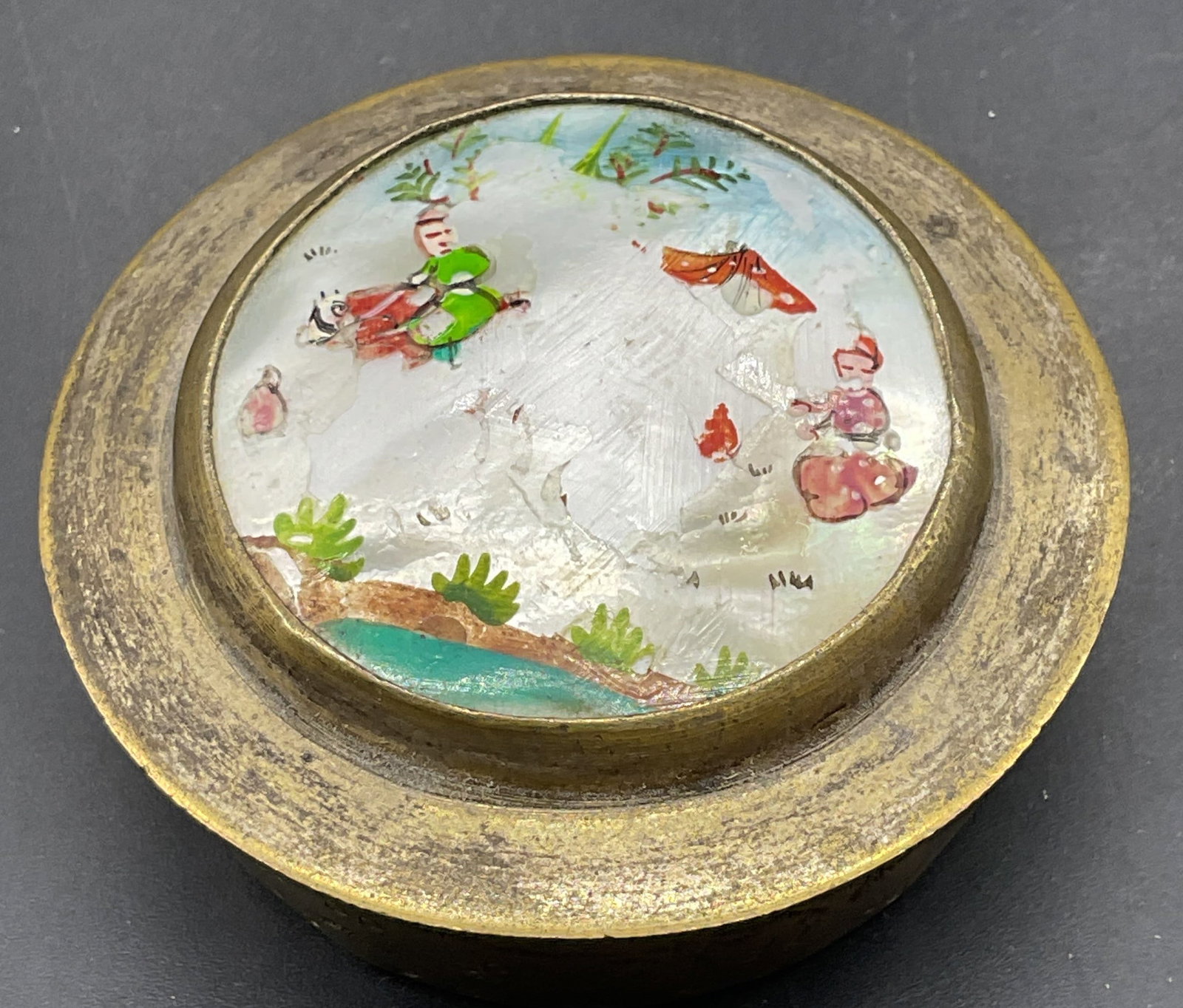Antique Asian Brass Mother of Pearl Trinket Box: Antique Asian silver plated brass trinket box with inlaid mother of pearl lid and hand painted figure scene. Mirror on interior lid. Measures approx. 2 x .75 inches. Wear including loss to paint,